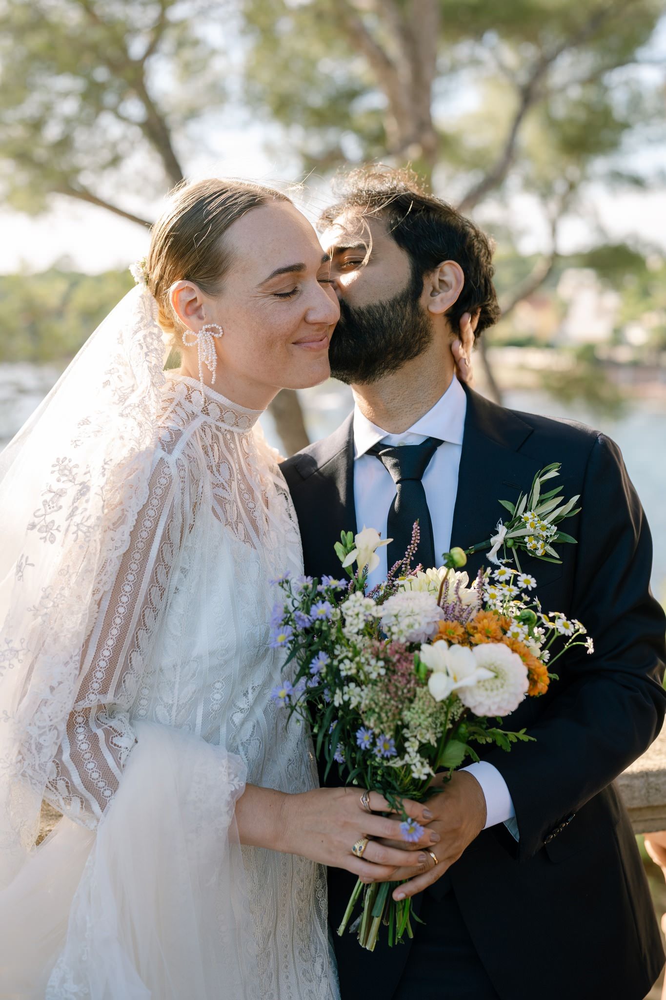 A tender wedding moment captured with a beautiful floral bouquet against a coastal background.