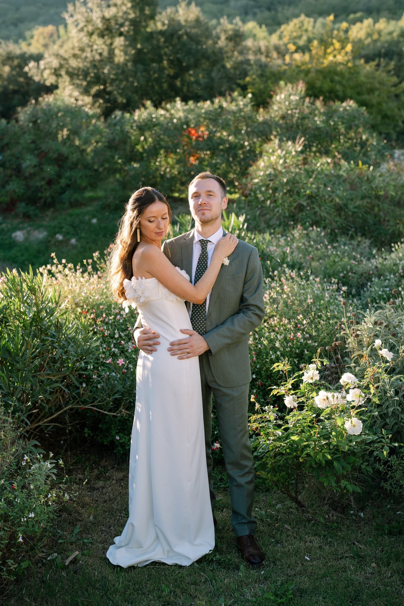 Newlyweds share intimate moments in a garden setting with blooming flowers.