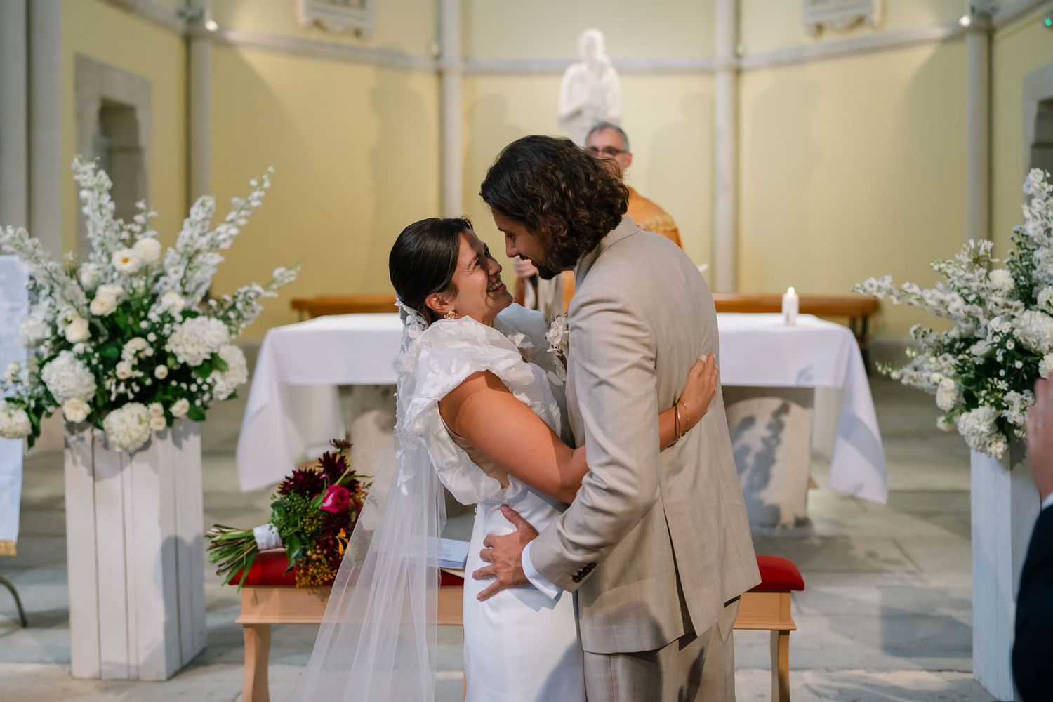 Wedding ceremony in a church with elegant white floral arrangements and soft yellow walls.