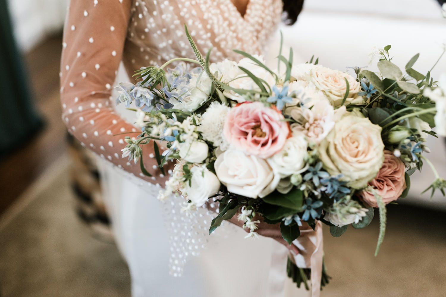 Romantic bridal bouquet featuring pink and white roses with blue accents and greenery.