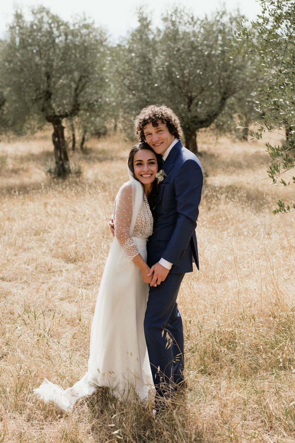 Romantic wedding couple embracing in a sun-lit olive grove.