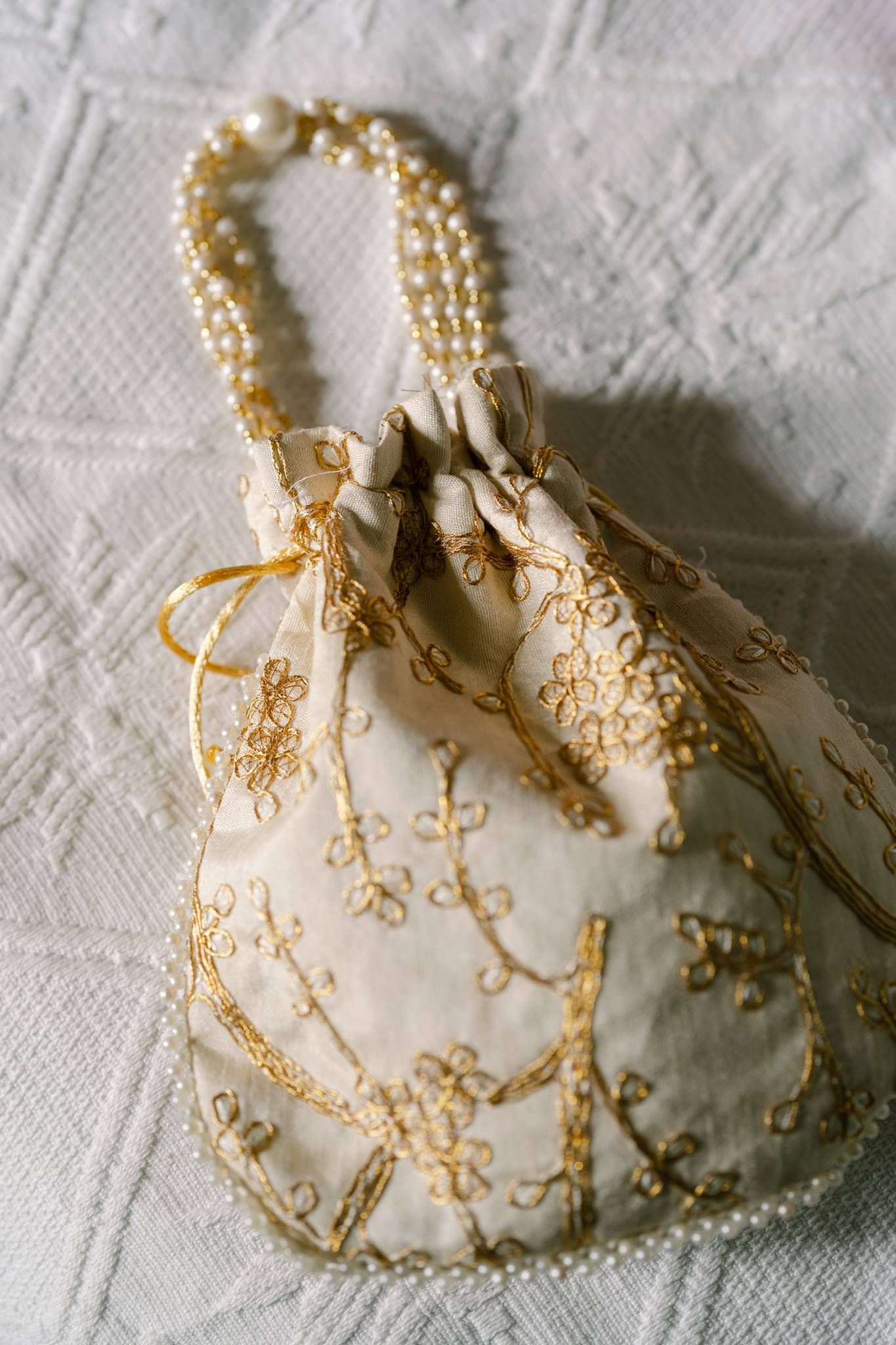 Delicate gold filigree detail on white fabric with intricate pearl embellishments.