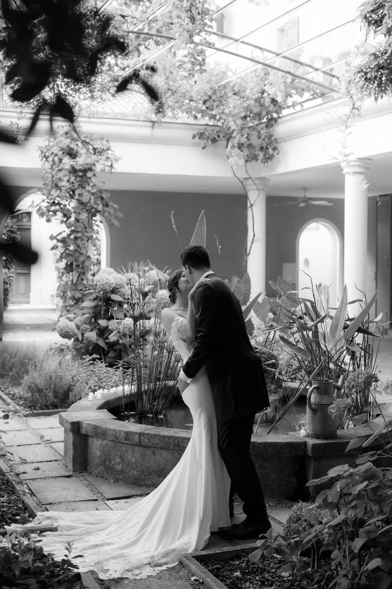 Black and white wedding photography in a garden courtyard with stone columns.