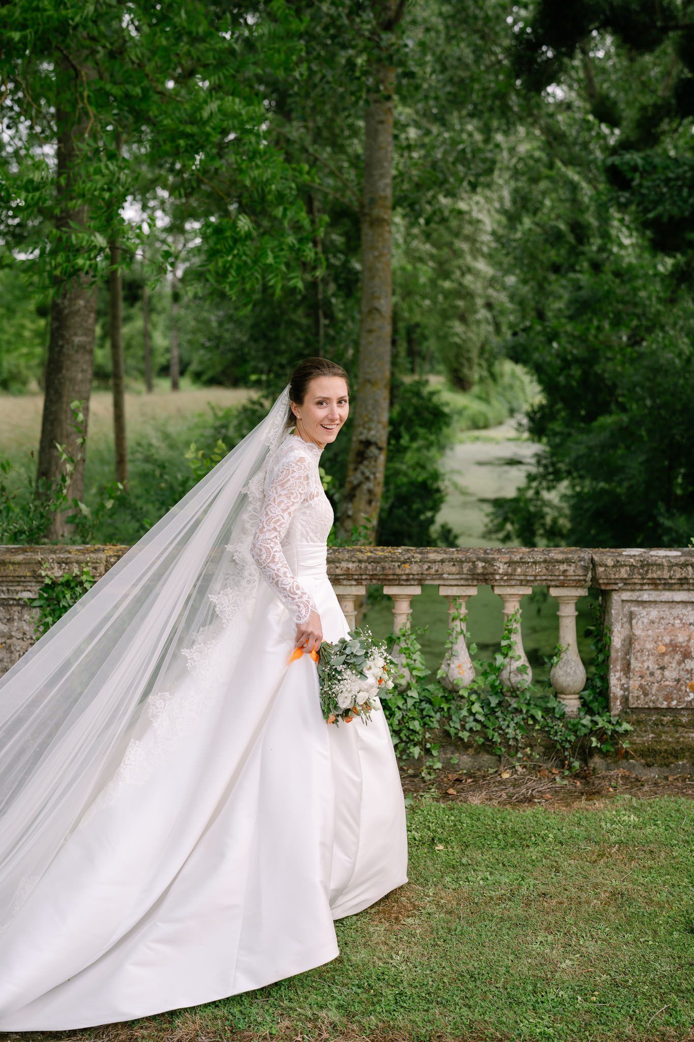 Elegant bride shows off flowing wedding dress train in lush garden setting.