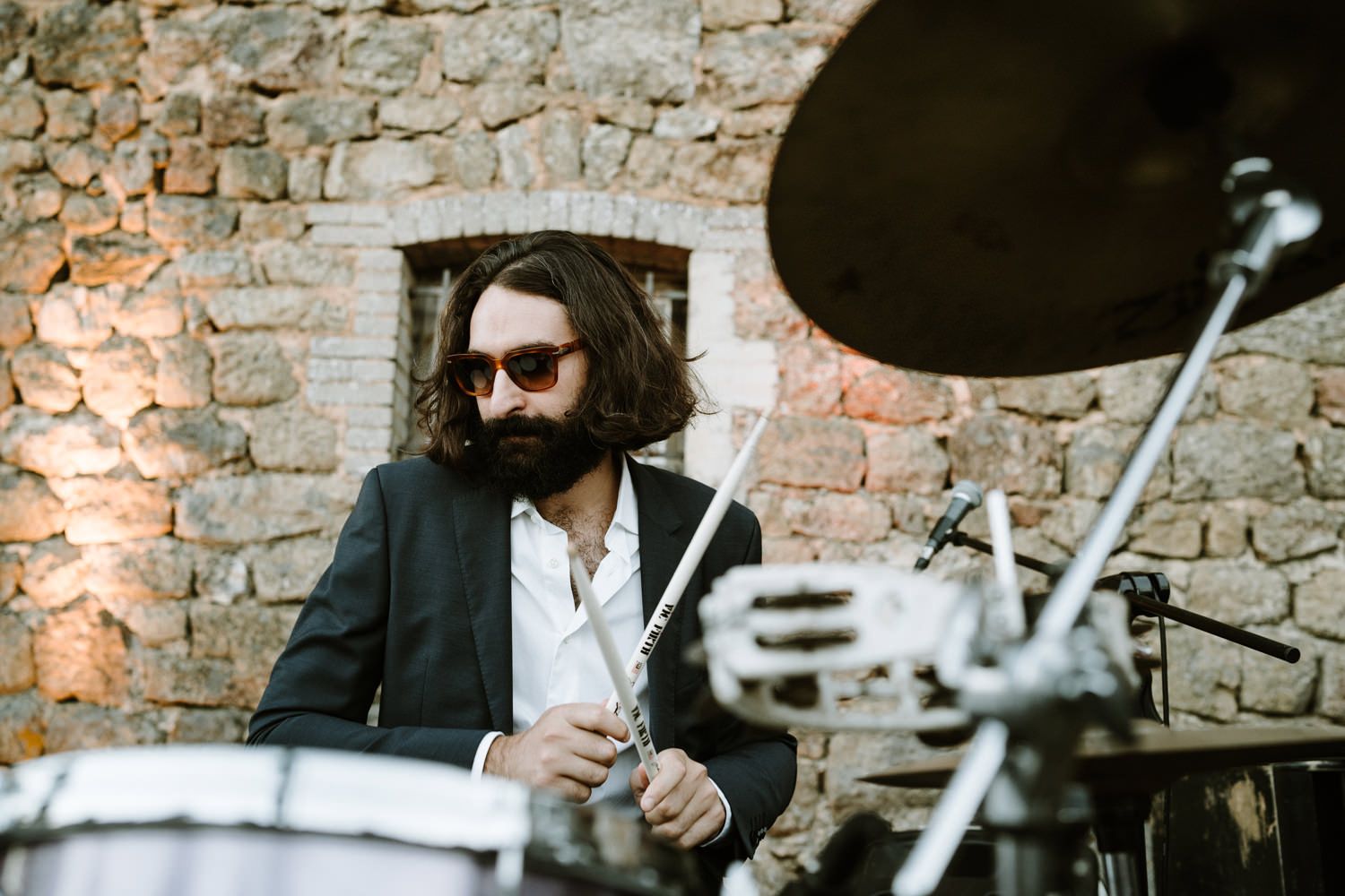 Band members playing instruments against rustic stone wall backdrop.