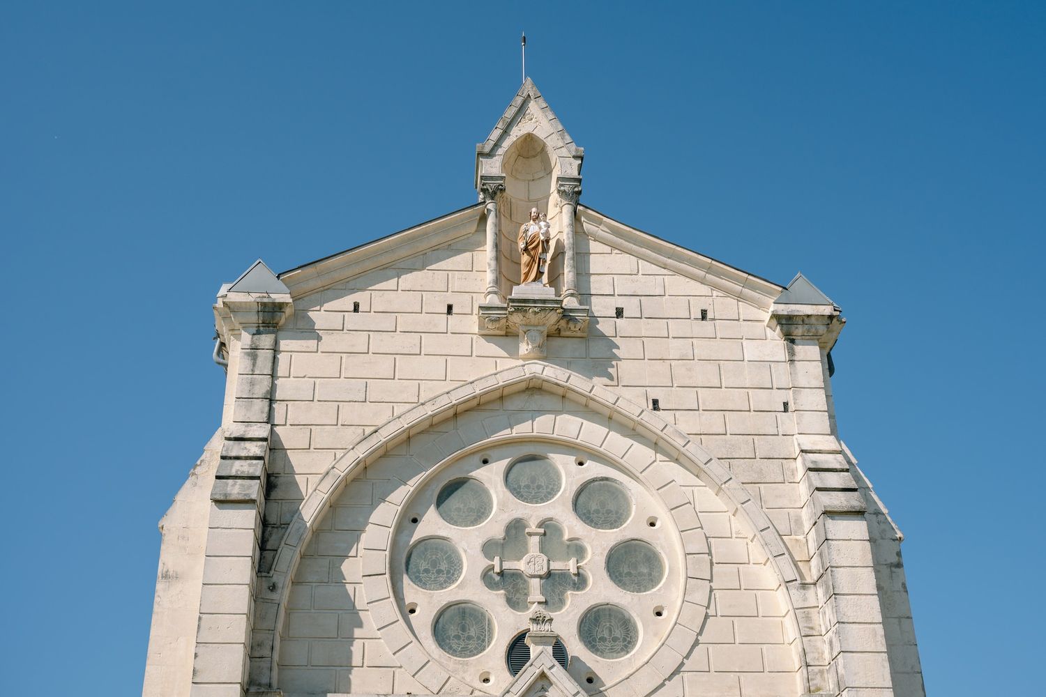 White stone church facade with circular rose window against bright blue sky.