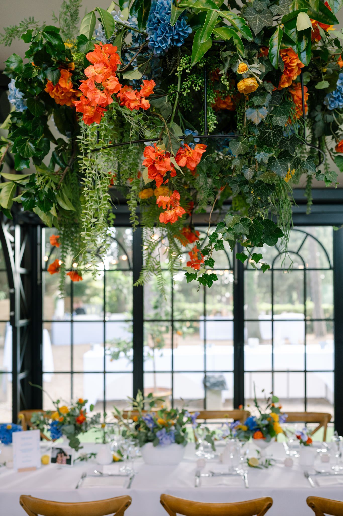 Vibrant orange flowers and greenery hang from ceiling above elegant reception tables.