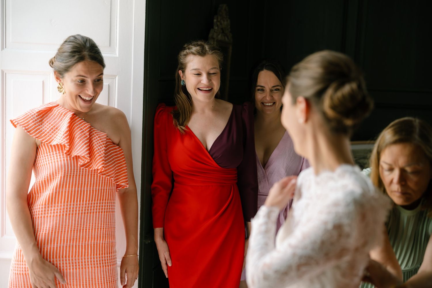 Wedding party in coral and red dresses helping with preparations.