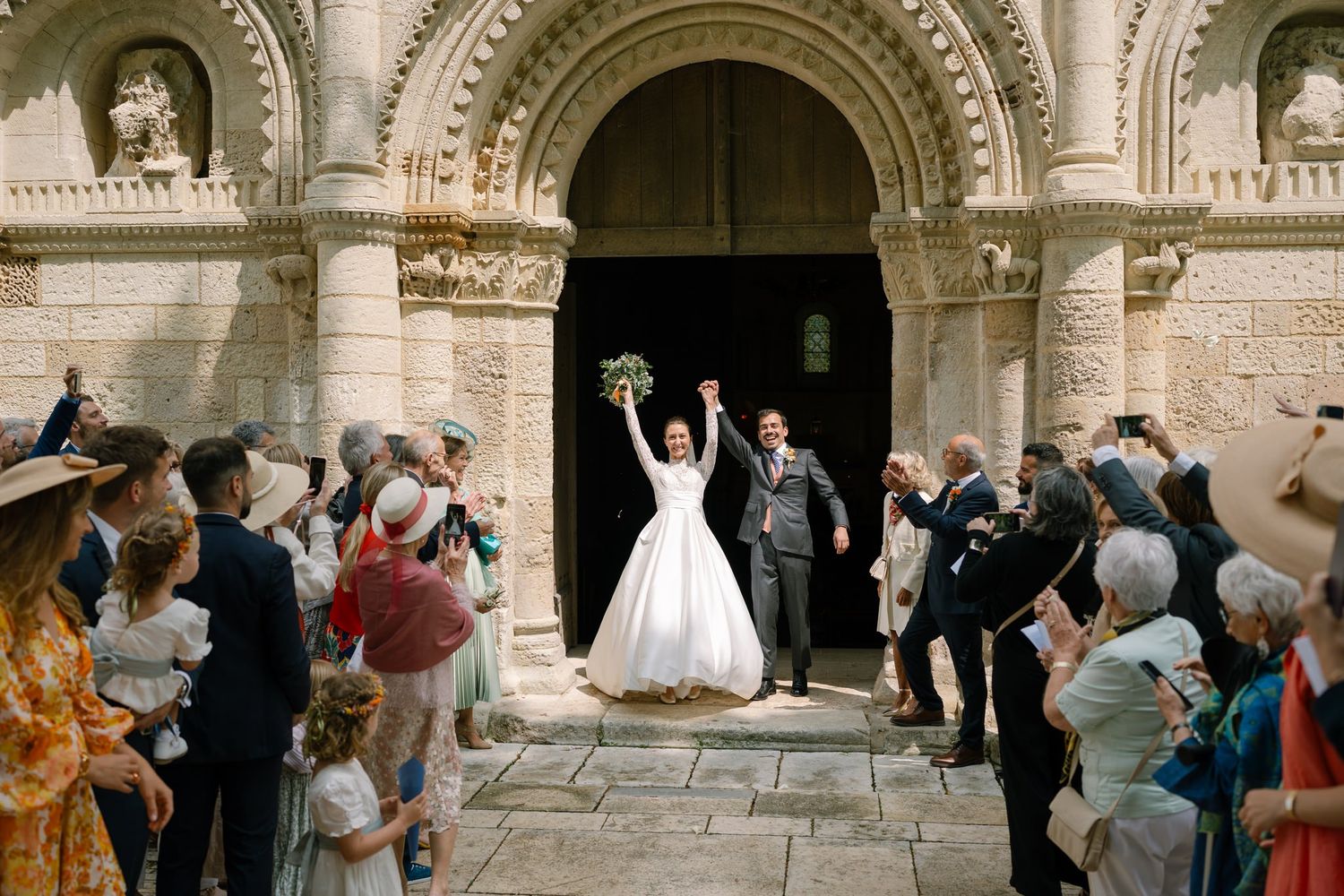 Wedding celebration outside historic stone church with ornate archways and columns.
