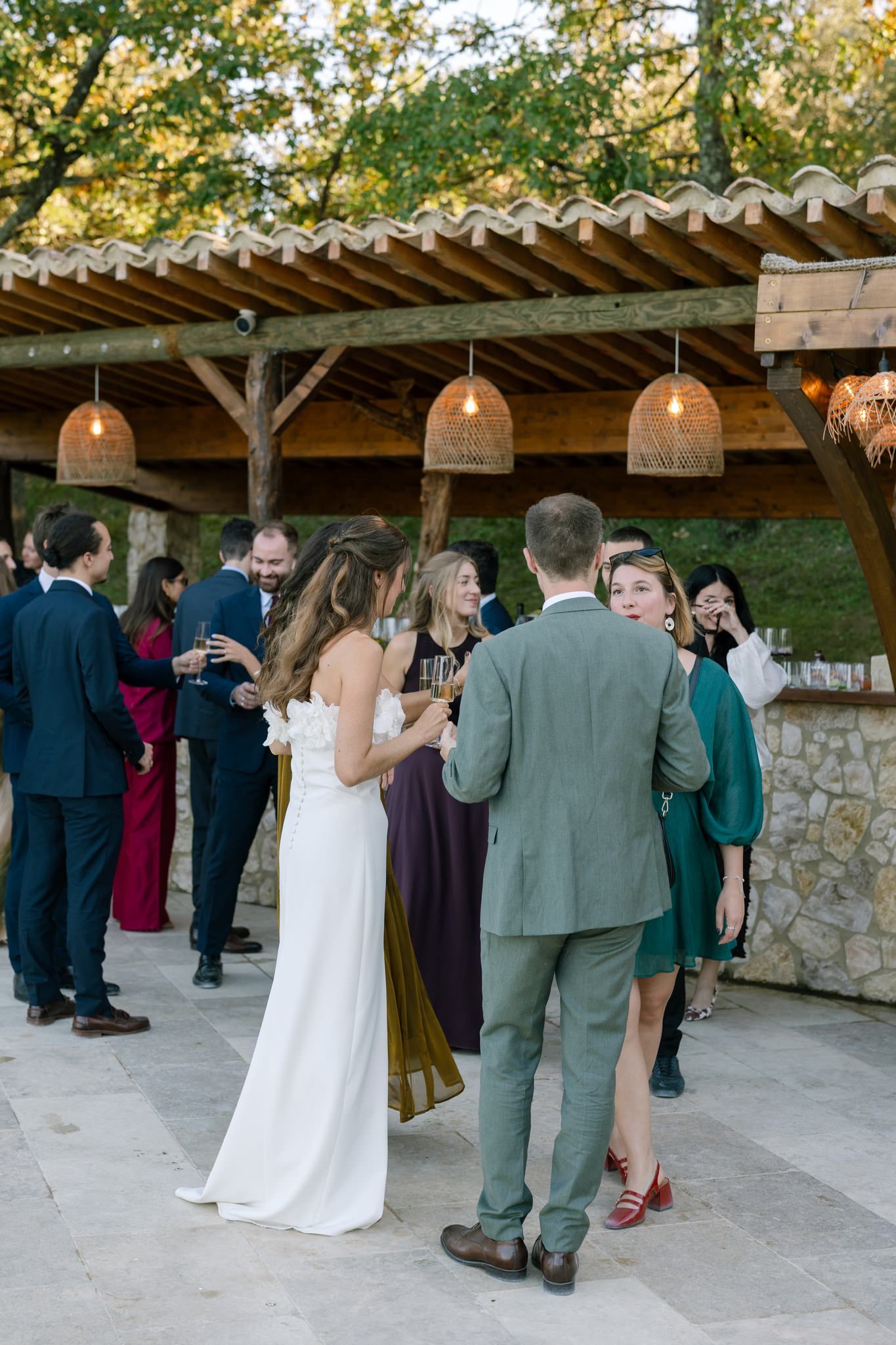 Wedding reception guests mingling under wooden pergola with woven pendant lights.