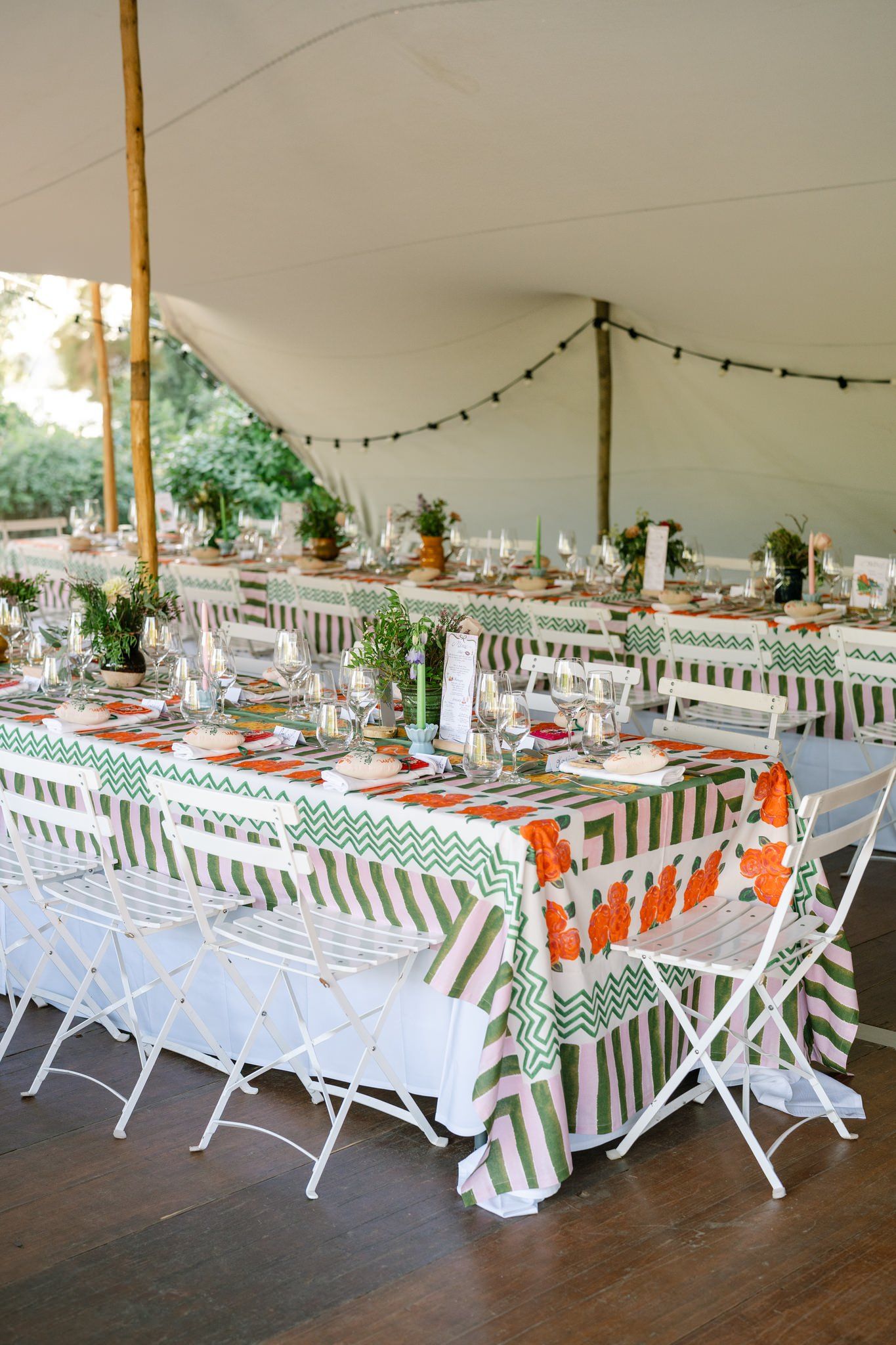 Long banquet tables with white chairs and striped tablecloths set under an outdoor tent.