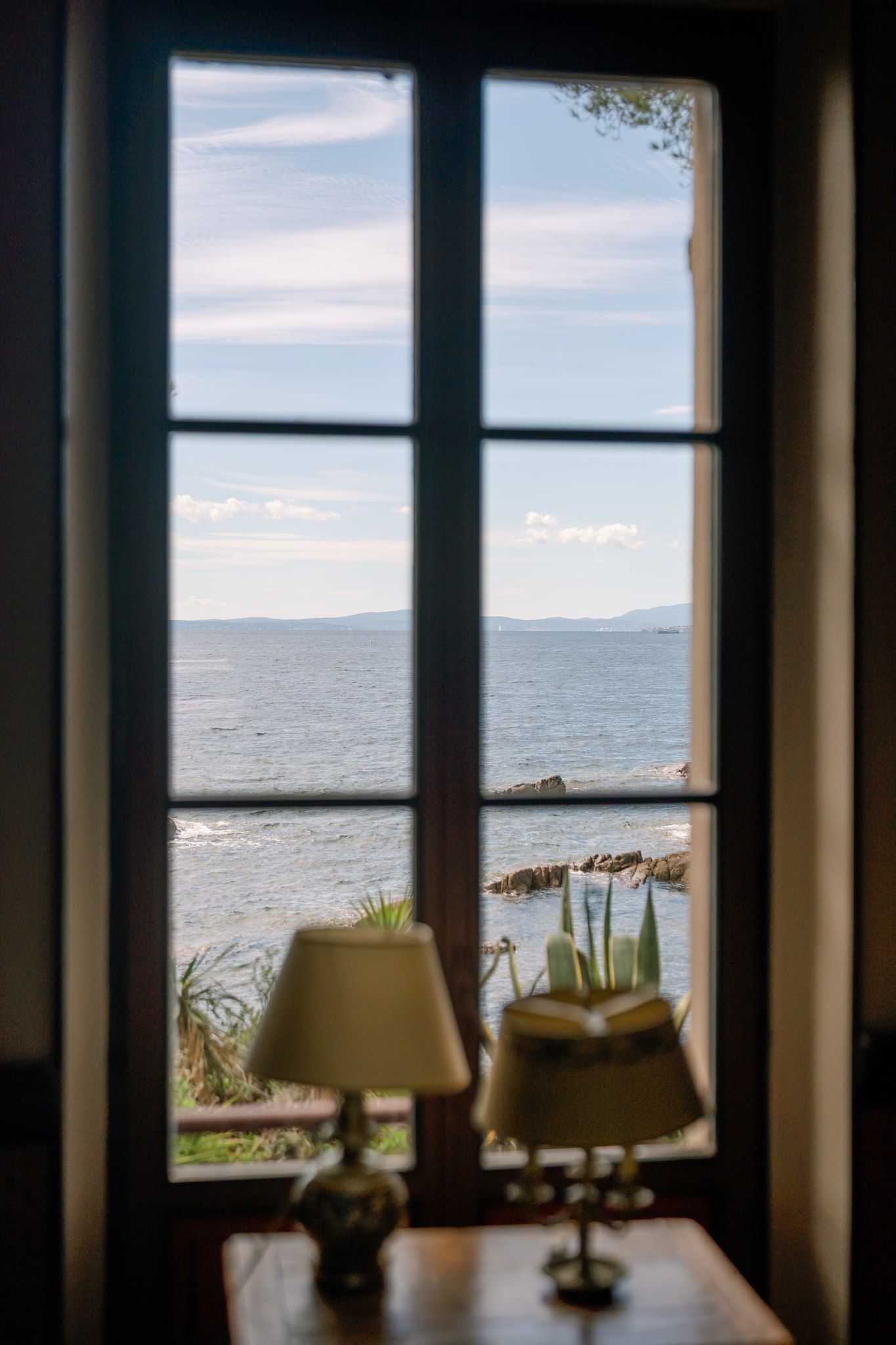 Ocean view through large windows with silhouetted furniture in the foreground.