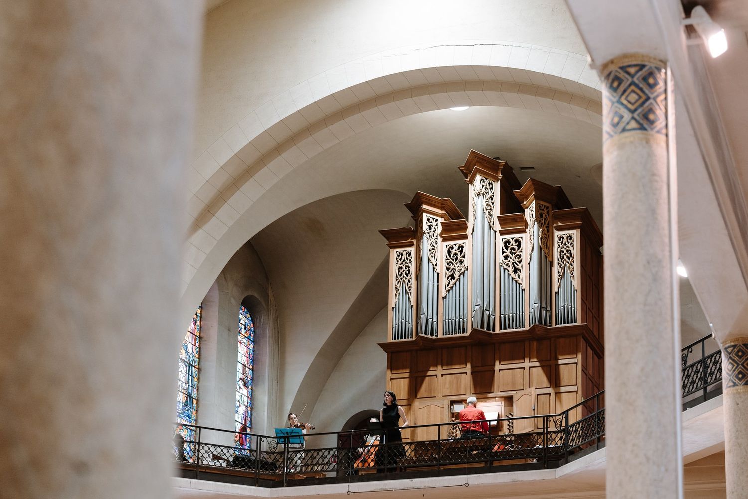View of church organ through arched doorway with stained glass windows.