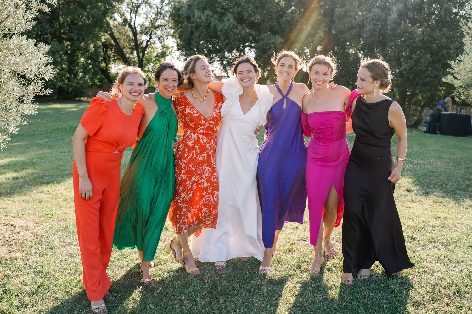 Wedding party members pose in vibrant colorful dresses outdoors.