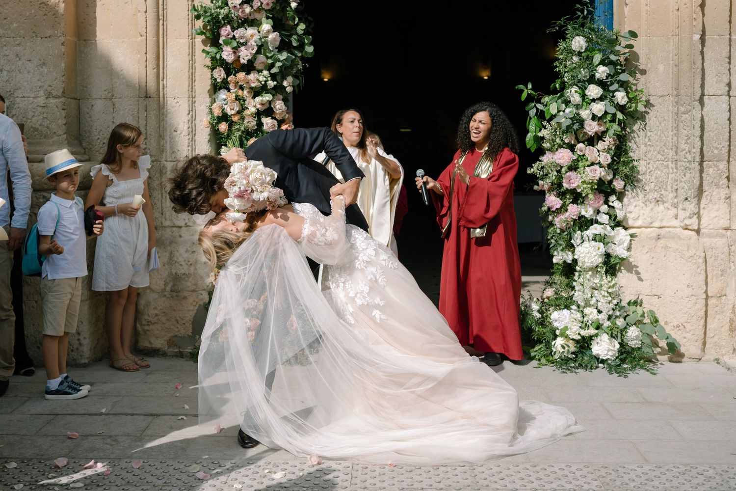 Wedding ceremony exit through ornate stone archway adorned with white floral arrangements.
