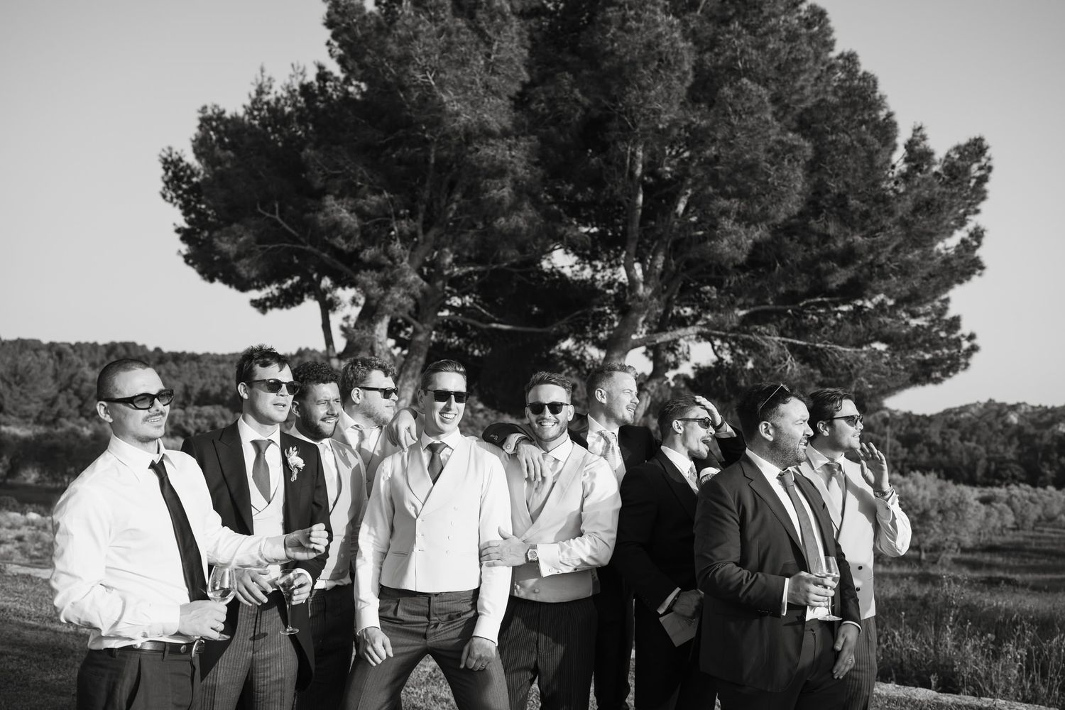 Wedding party poses for group photos outdoors under tall pine trees.