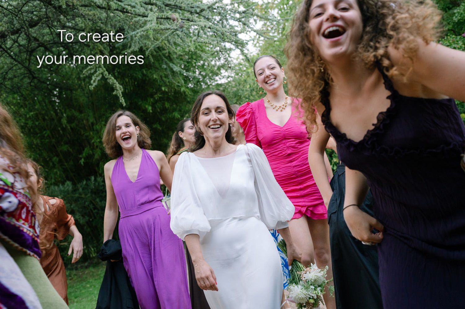 A group in purple and pink dresses laughs together while walking outdoors in a garden setting.