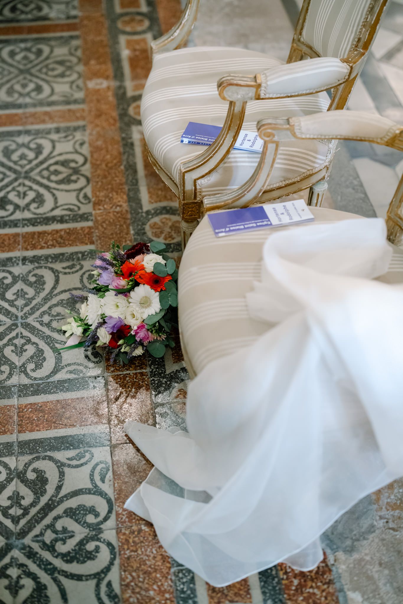 Elegant white chairs with floral decorations arranged on ornate tiled flooring.