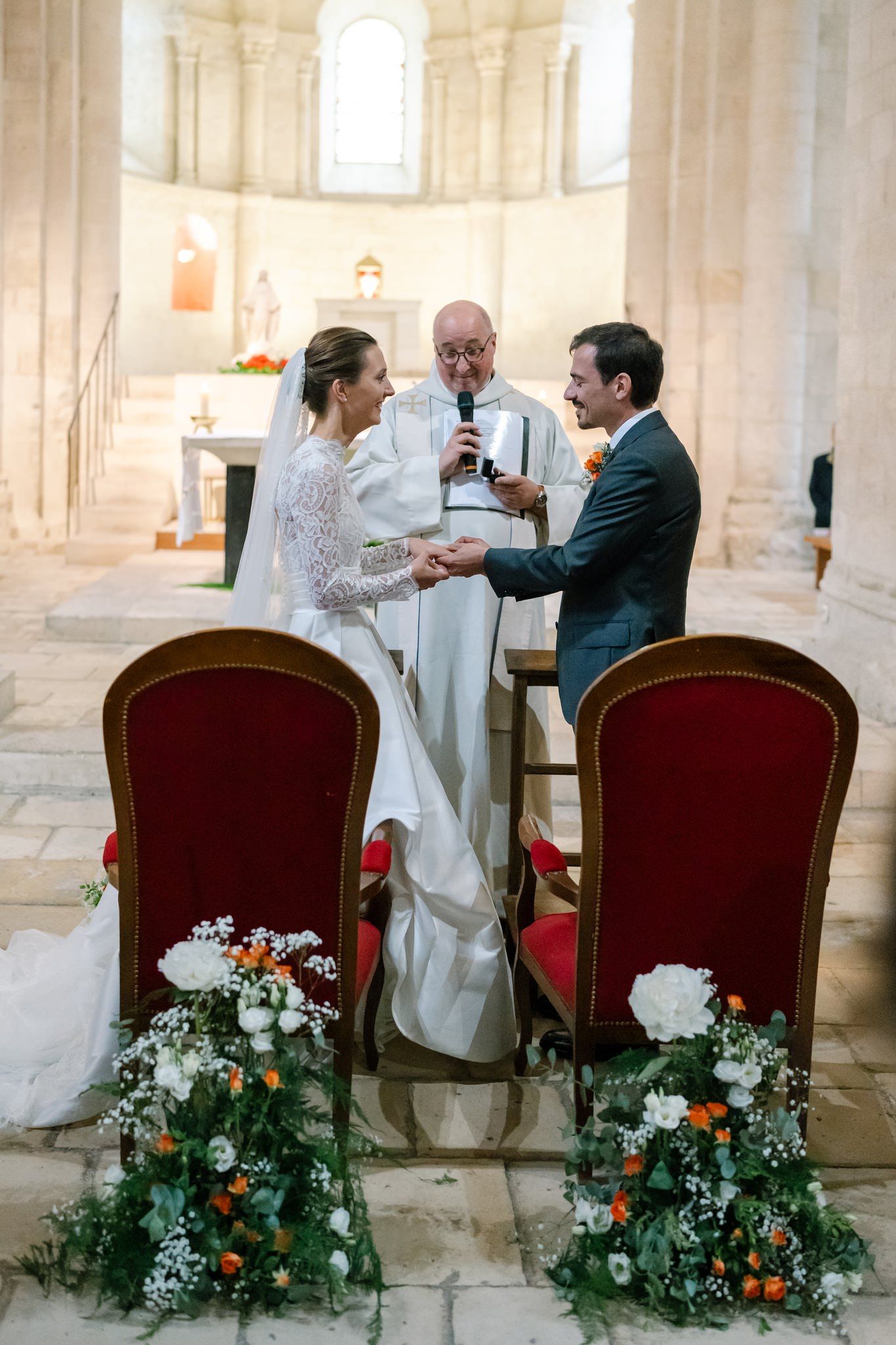 Elegant wedding ceremony chairs adorned with floral arrangements in a bright church setting.
