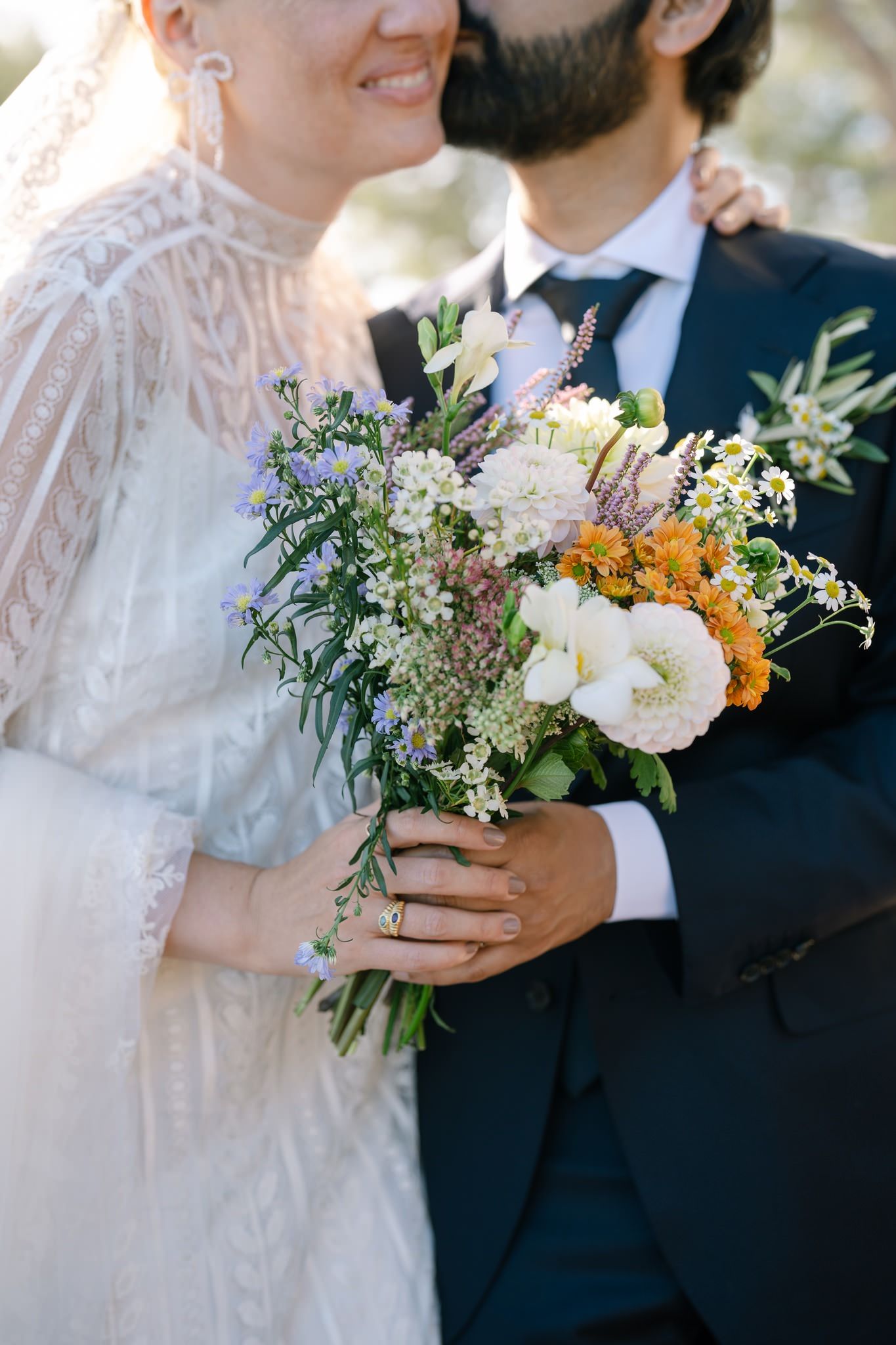 Close-up of wedding bouquet with white and orange flowers held against lace dress.