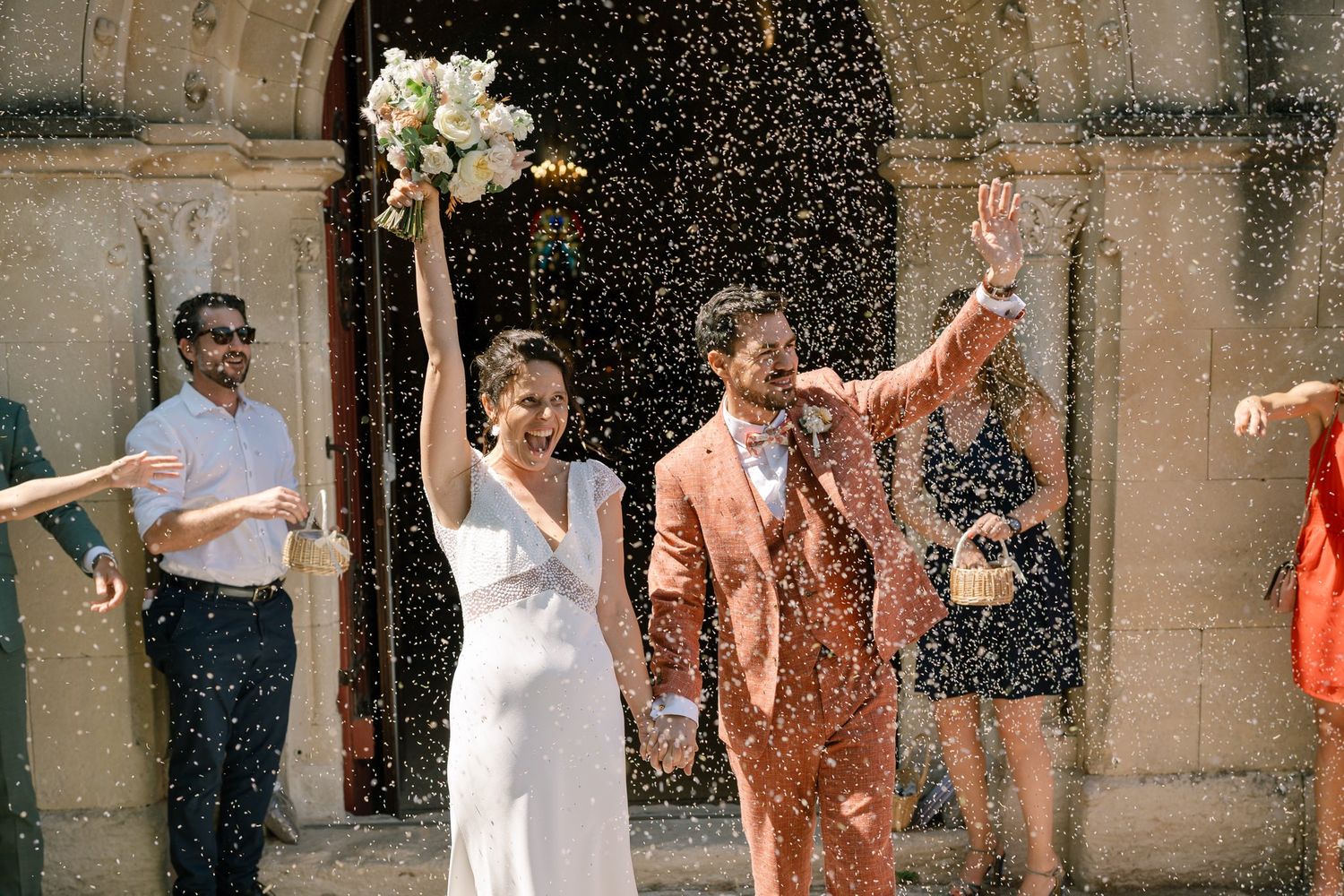 Wedding party celebrating with confetti outside historic stone building.