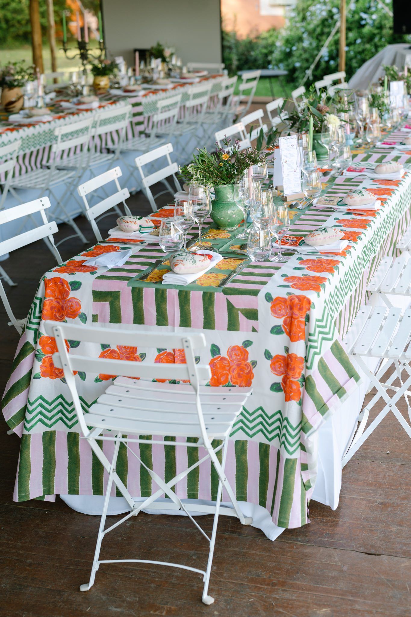 Wedding reception tables set with green striped linens and orange floral accents under a covered outdoor space.