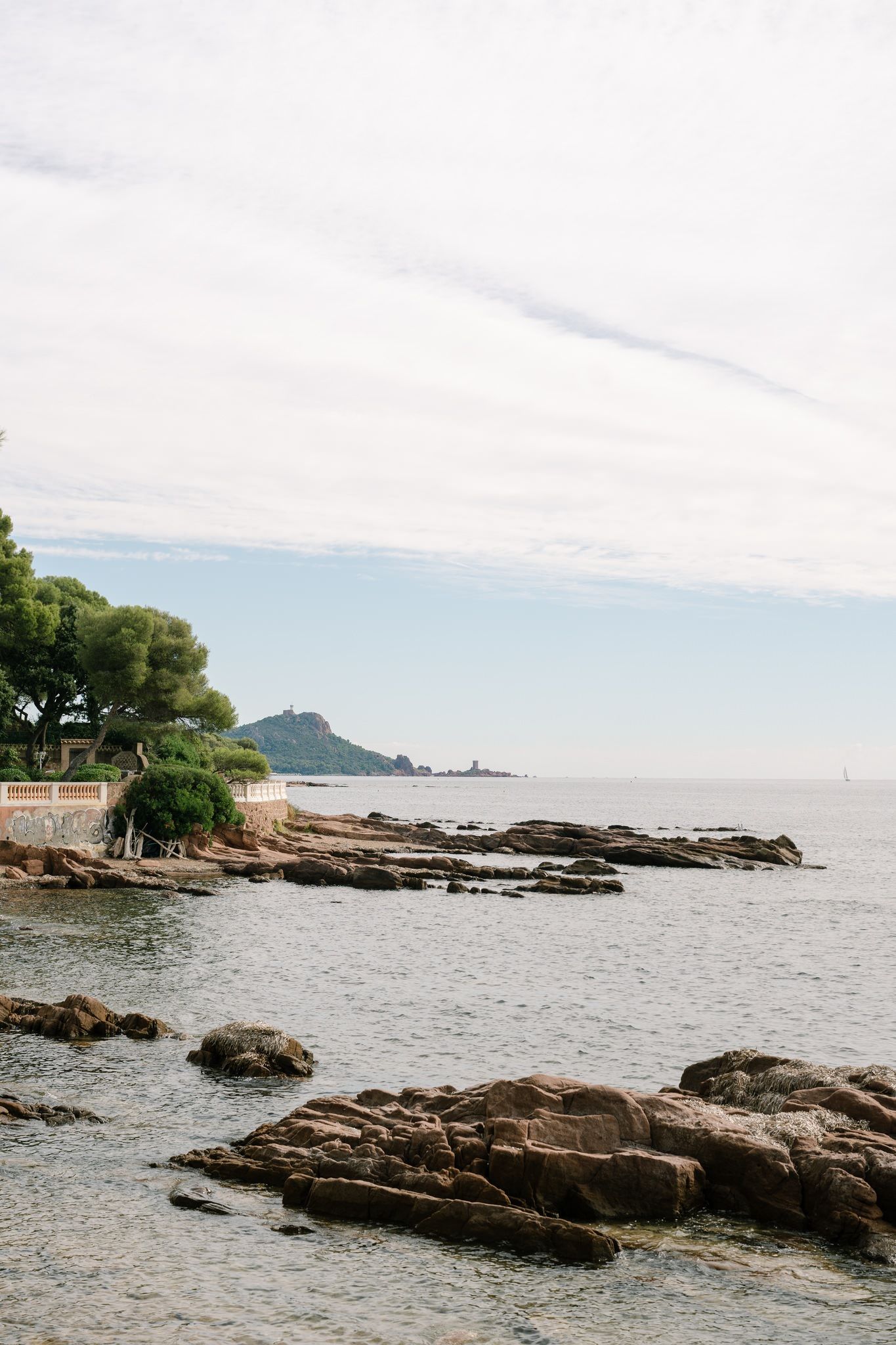 Rocky coastline with clear blue waters and distant islands on the horizon.