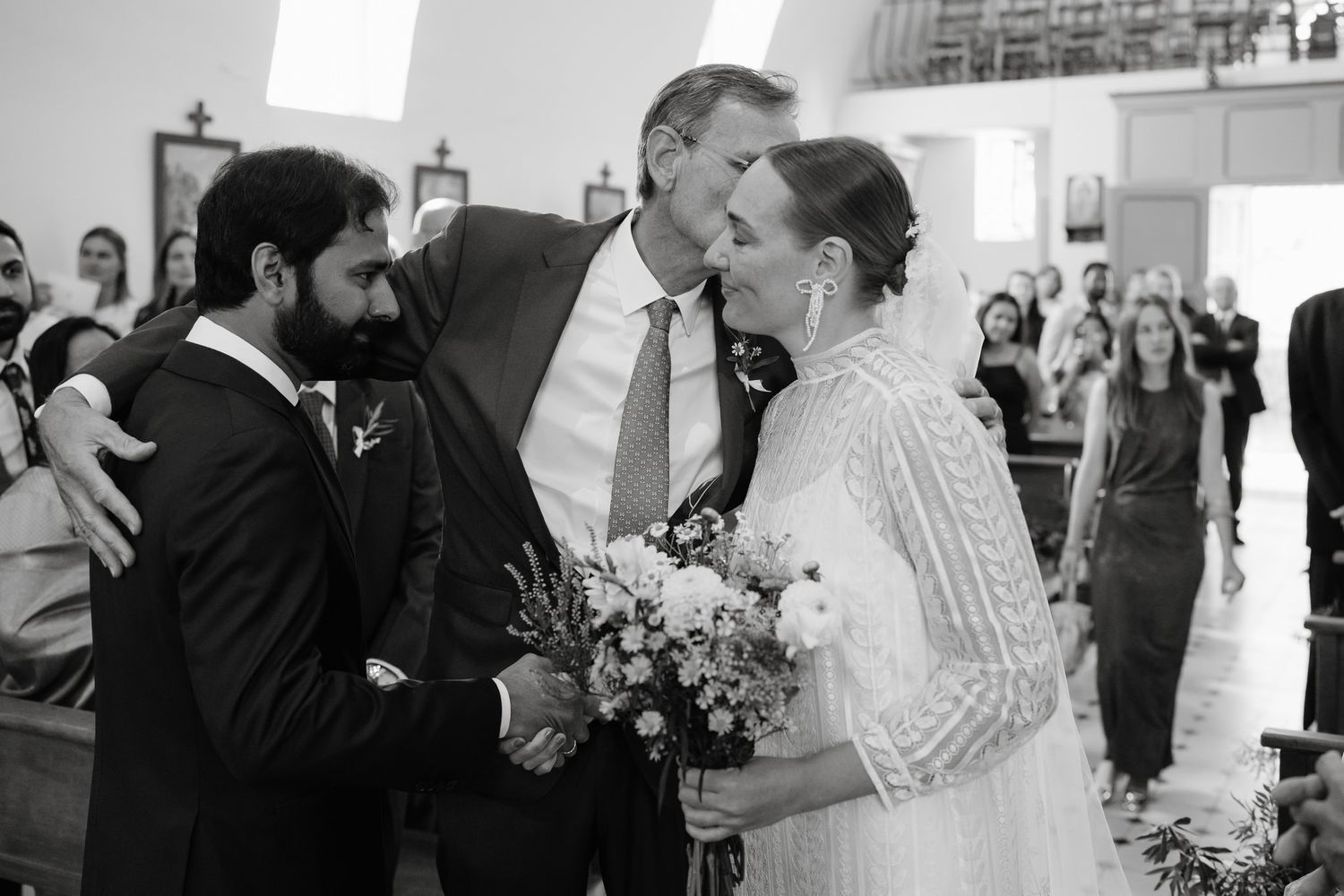 Wedding party exchanges greetings and embraces during church ceremony.