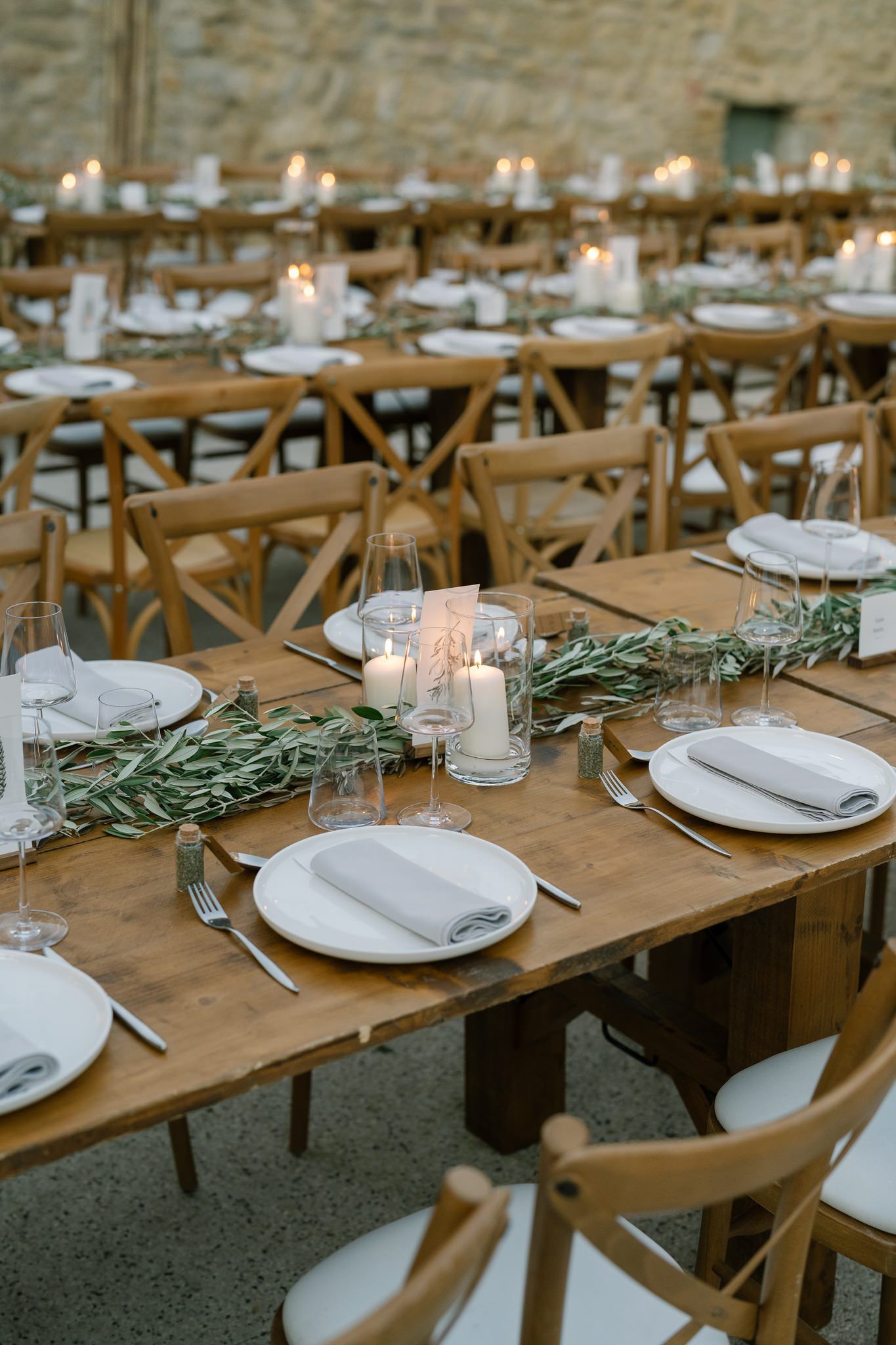 Rustic wooden tables set for a wedding reception with white plates and olive branch decorations.