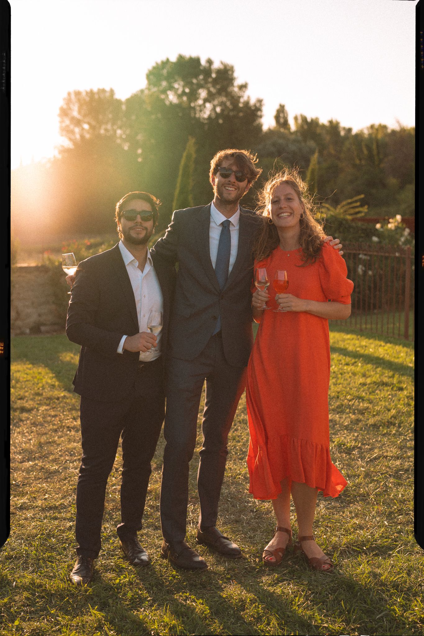 Group in formal attire poses together on grassy hill during golden hour sunset.