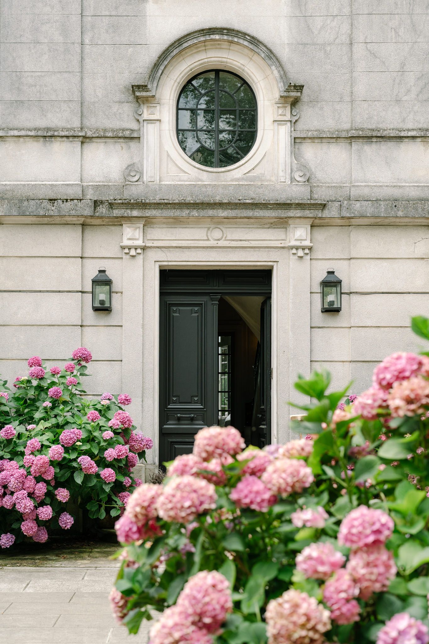 Pink hydrangeas bloom beautifully along a classic stone building entrance with dark doors.