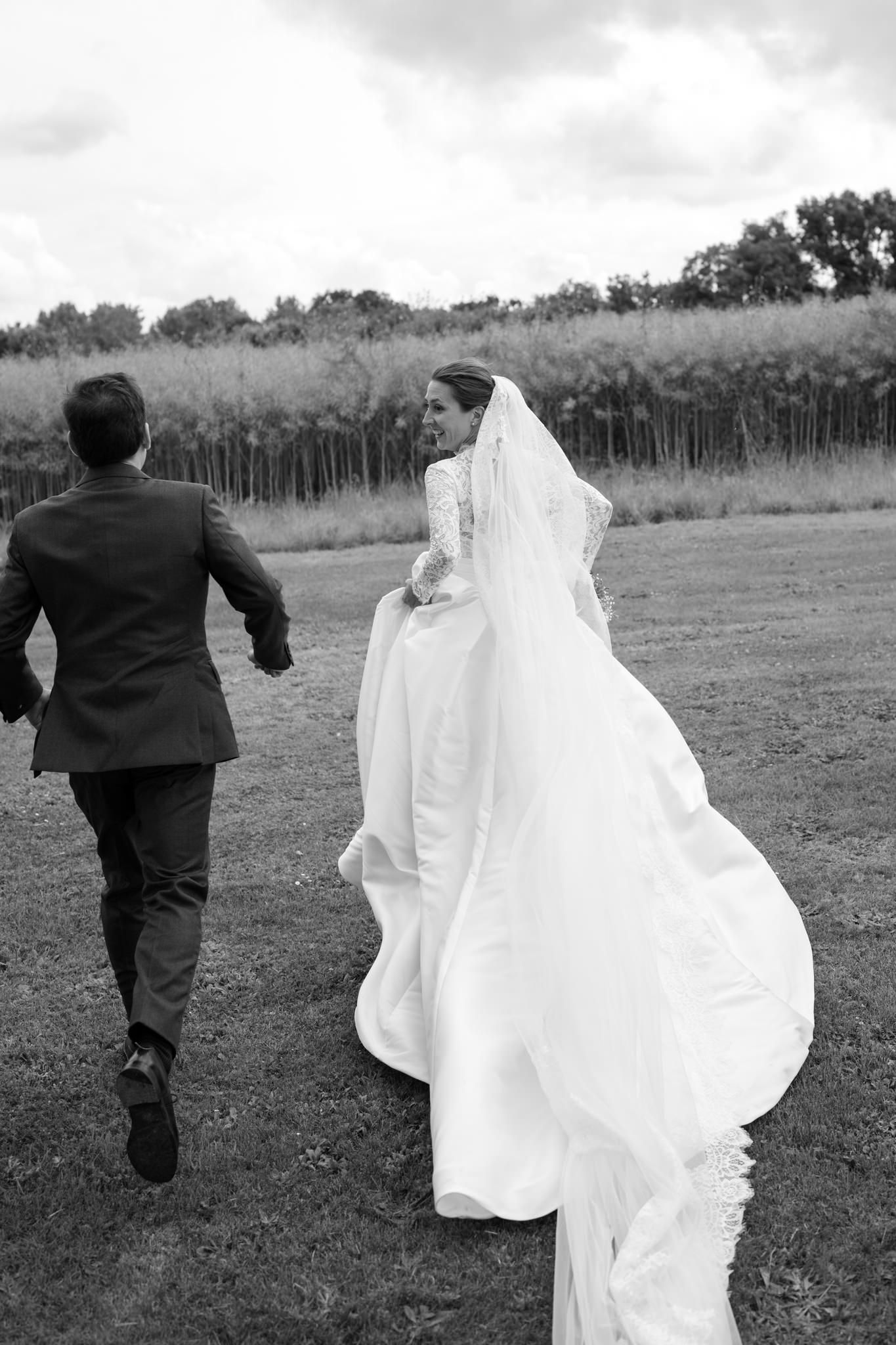 Wedding couple runs playfully across an open field in black and white photography.