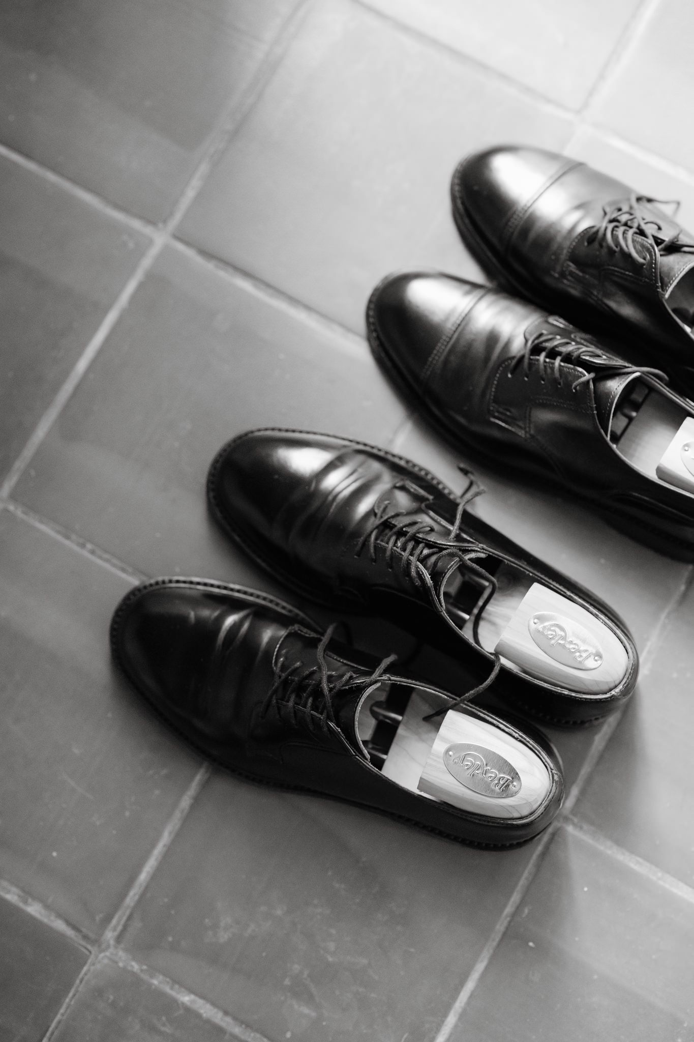 Black formal leather dress shoes arranged in a row on grey tile flooring.