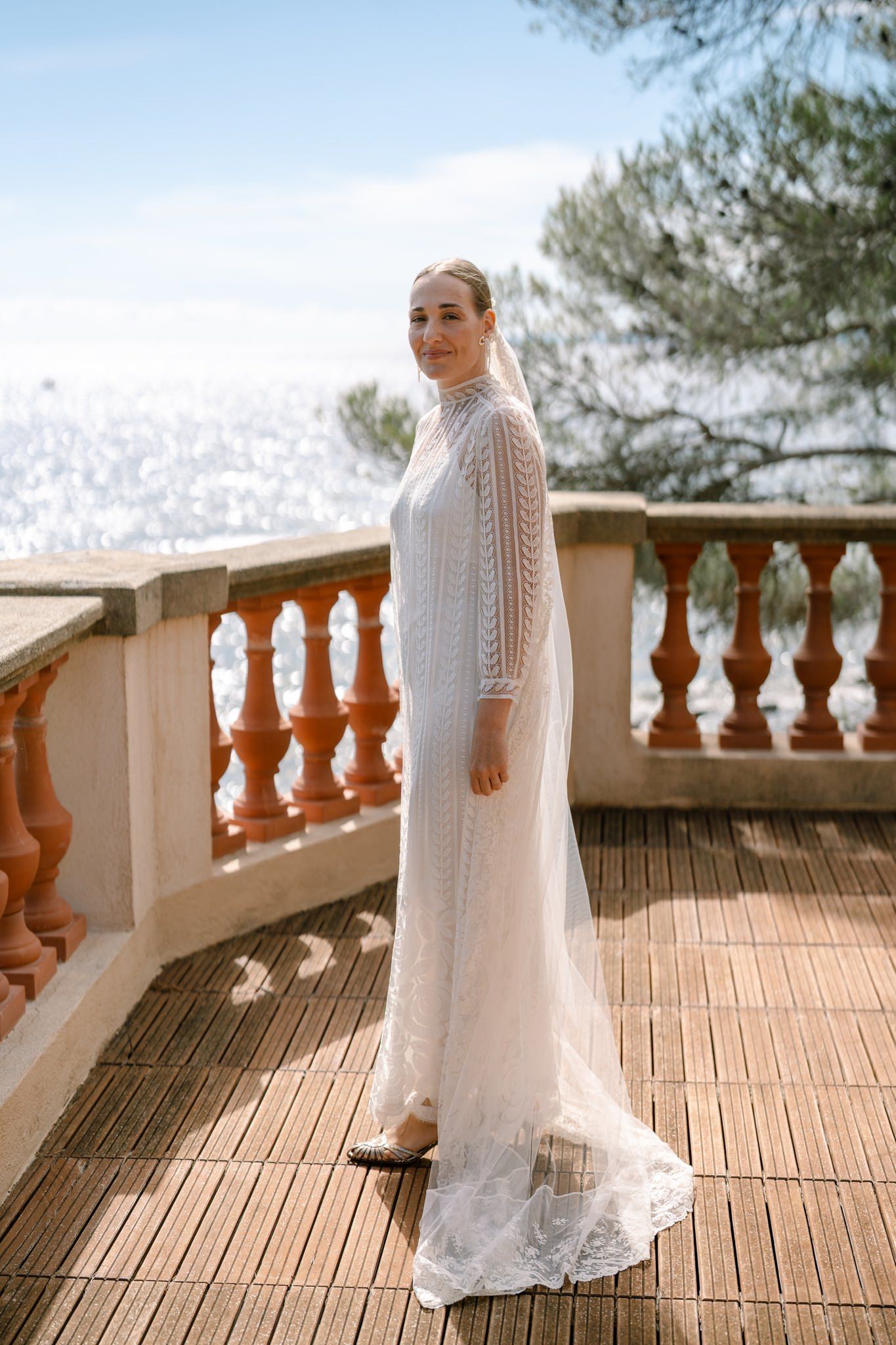 Bride in a vintage-style lace dress poses on a terracotta balcony with ornate balusters.