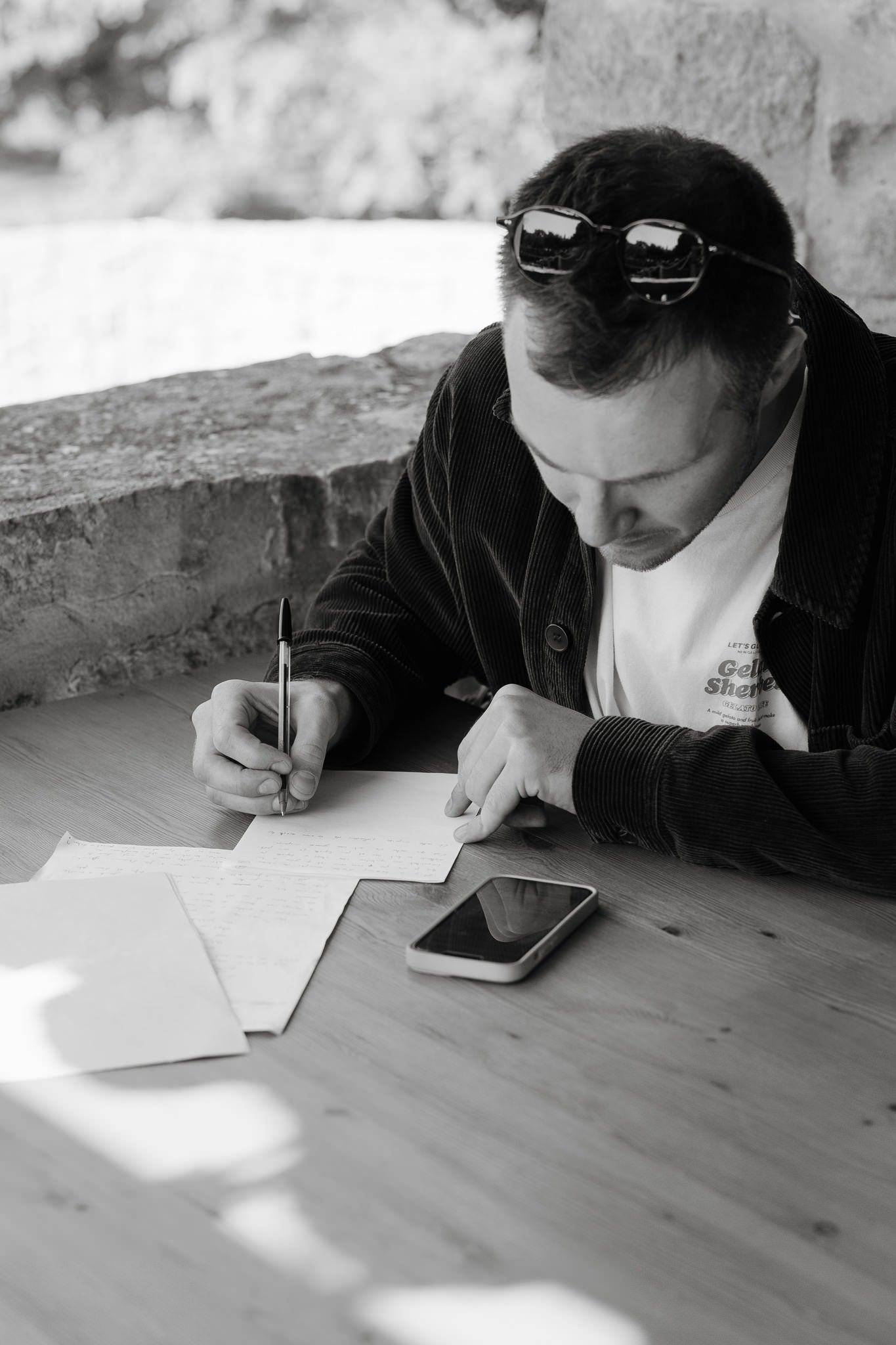 People writing and working at a wooden table, captured in black and white photography.