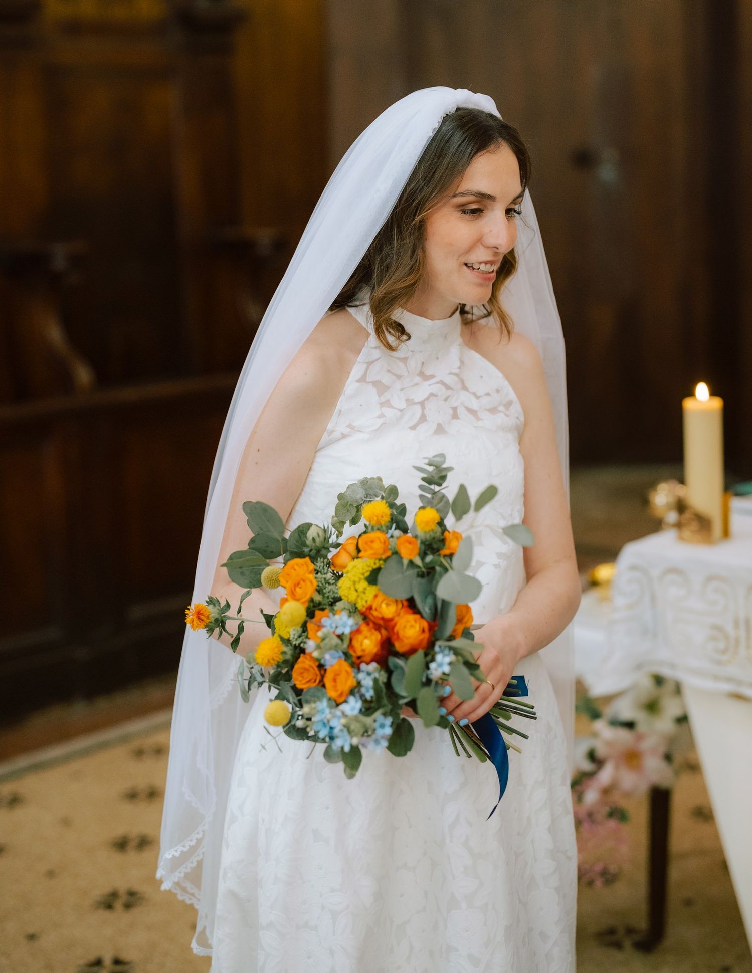 Wedding dress detail with vibrant orange and yellow floral bouquet against rustic wooden background.