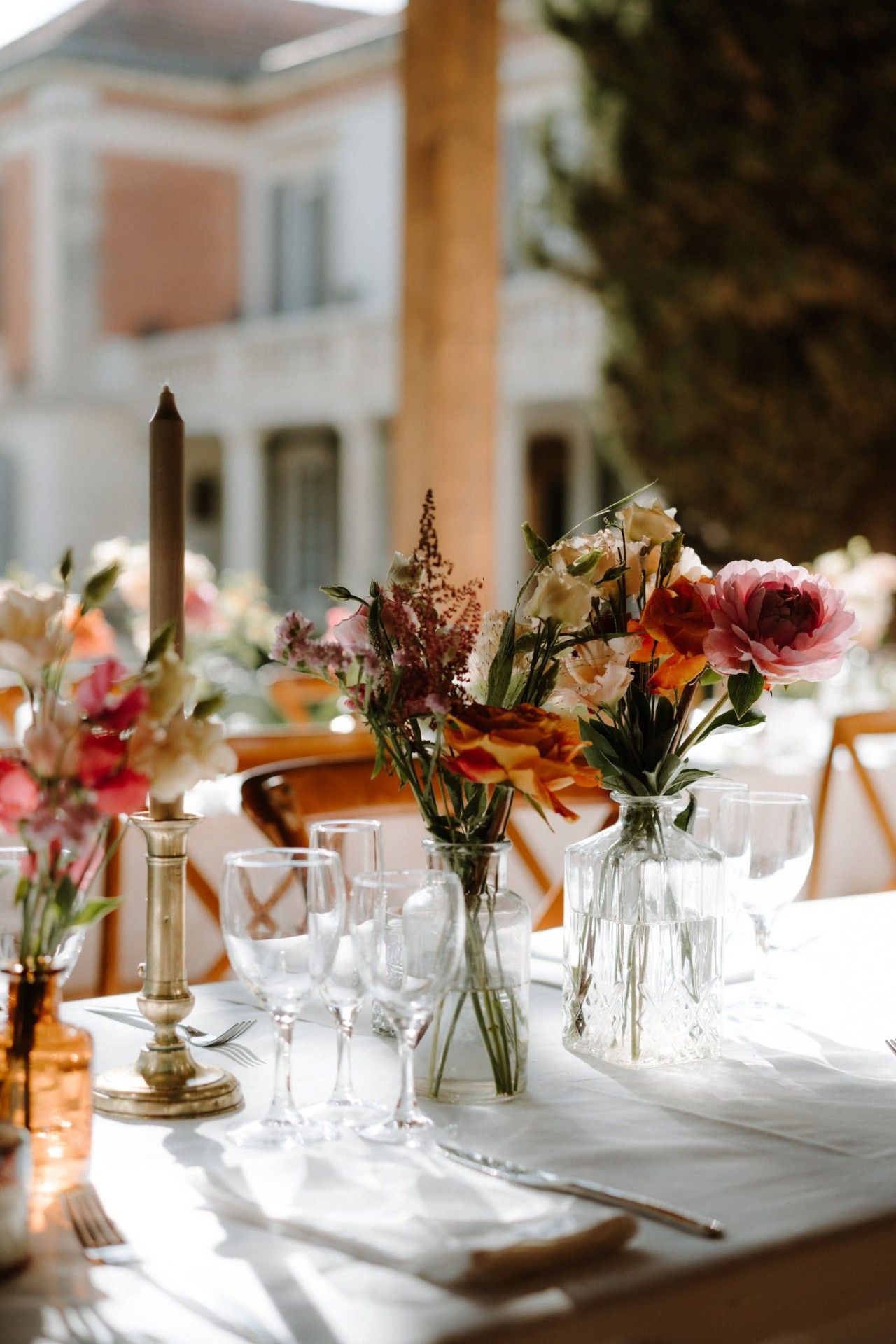 Wedding table centerpieces with colorful flowers in small vases on white tablecloth.