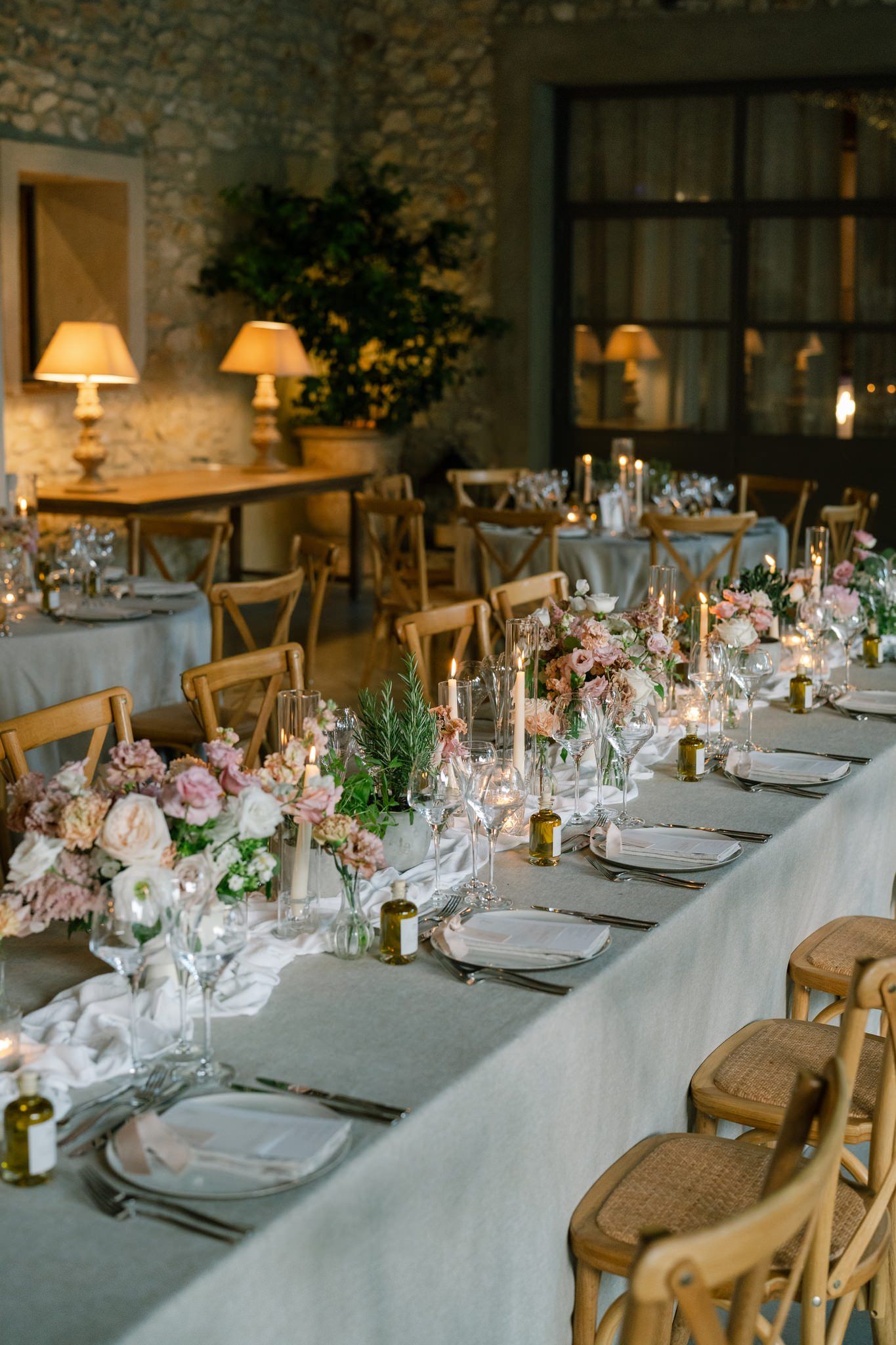 Elegant wedding reception table setting with rustic wooden chairs and soft floral centerpieces in a stone-walled venue.