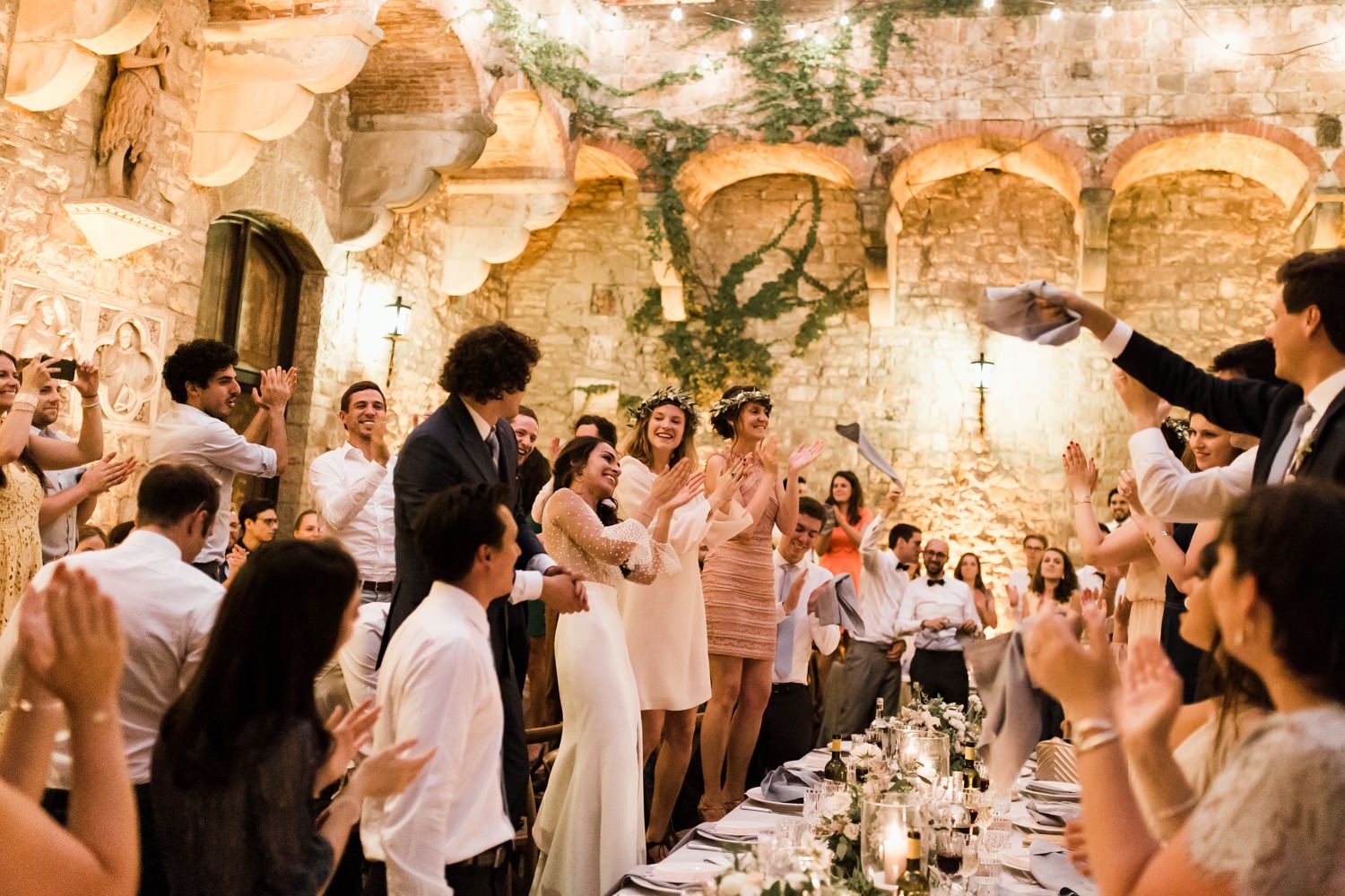 Wedding reception celebration in rustic stone venue with guests cheering.