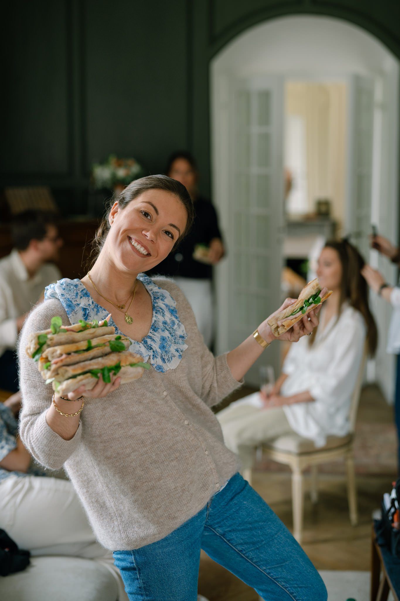 Person in blue and grey sweater enjoying sandwiches at an indoor gathering.