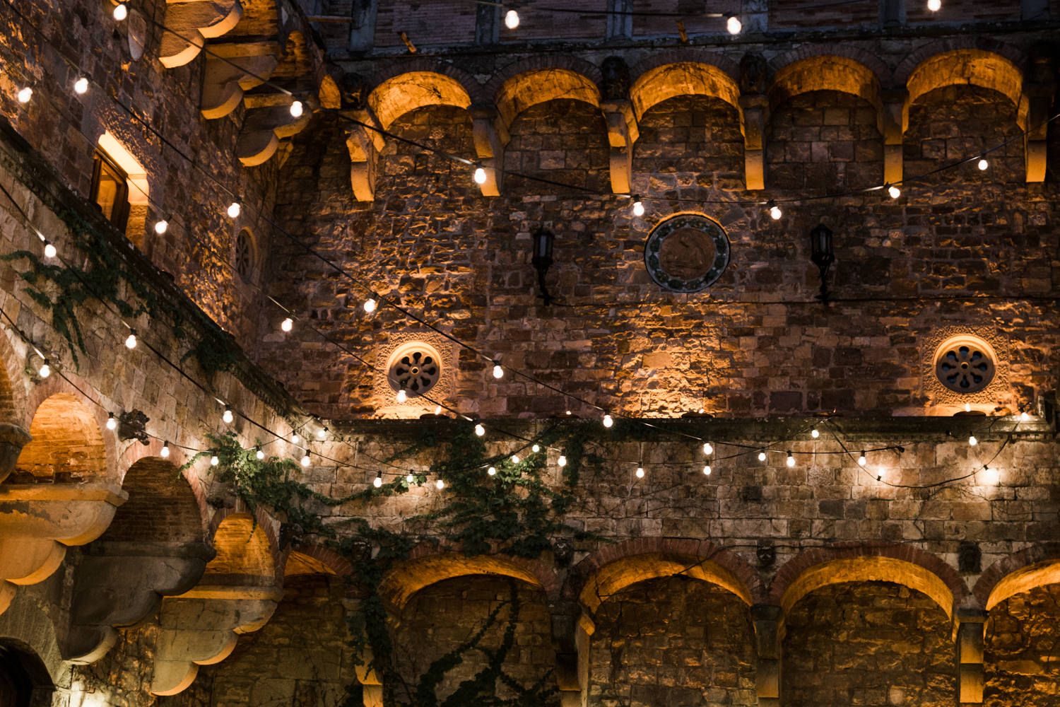 Stone castle wall with illuminated arches and string lights creating romantic ambiance.