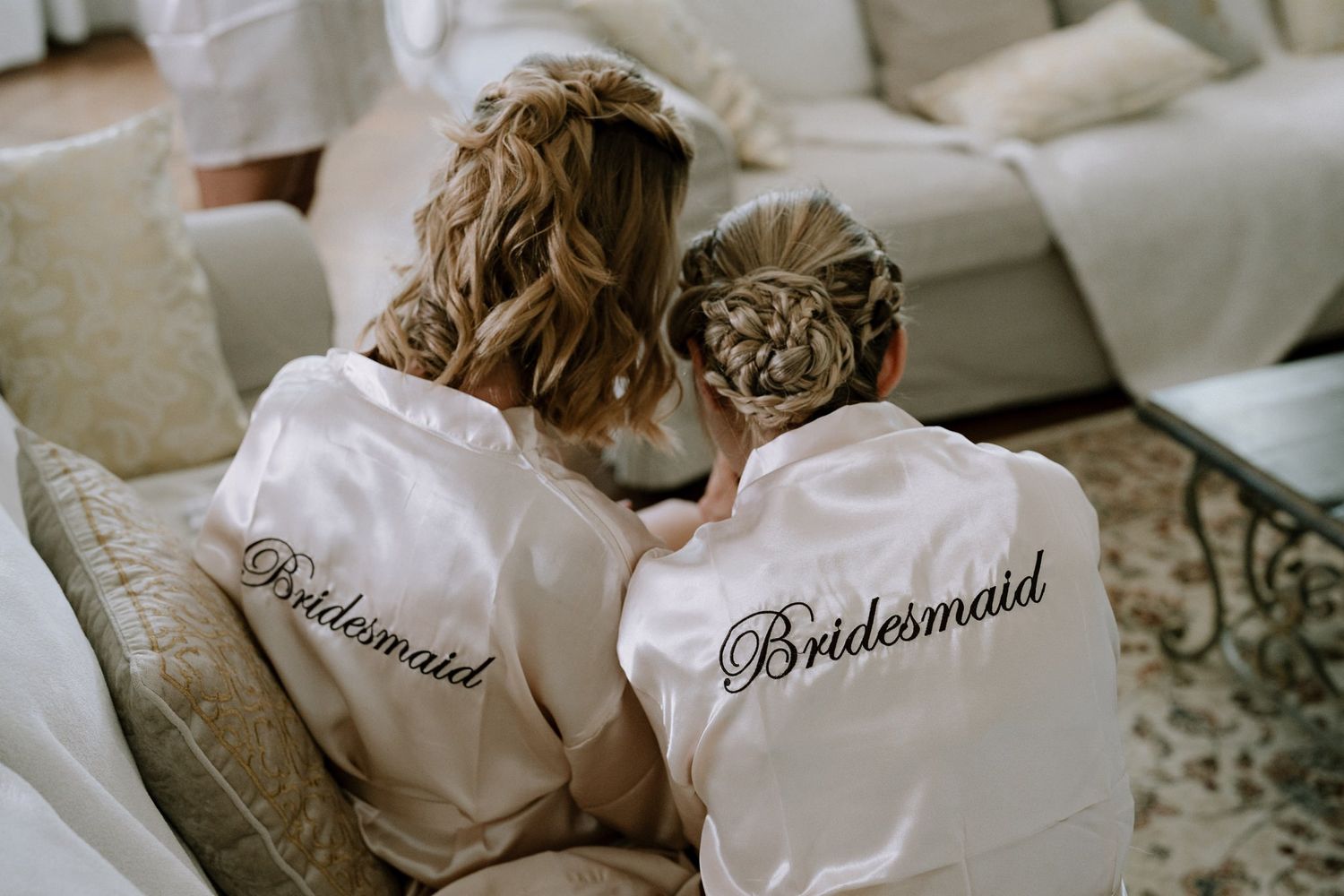 White silk robes with 'Bridesmaid' embroidery laid out for wedding preparation.
