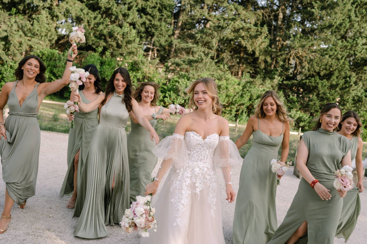 Wedding party in sage green dresses celebrating outdoors with joyful expressions.