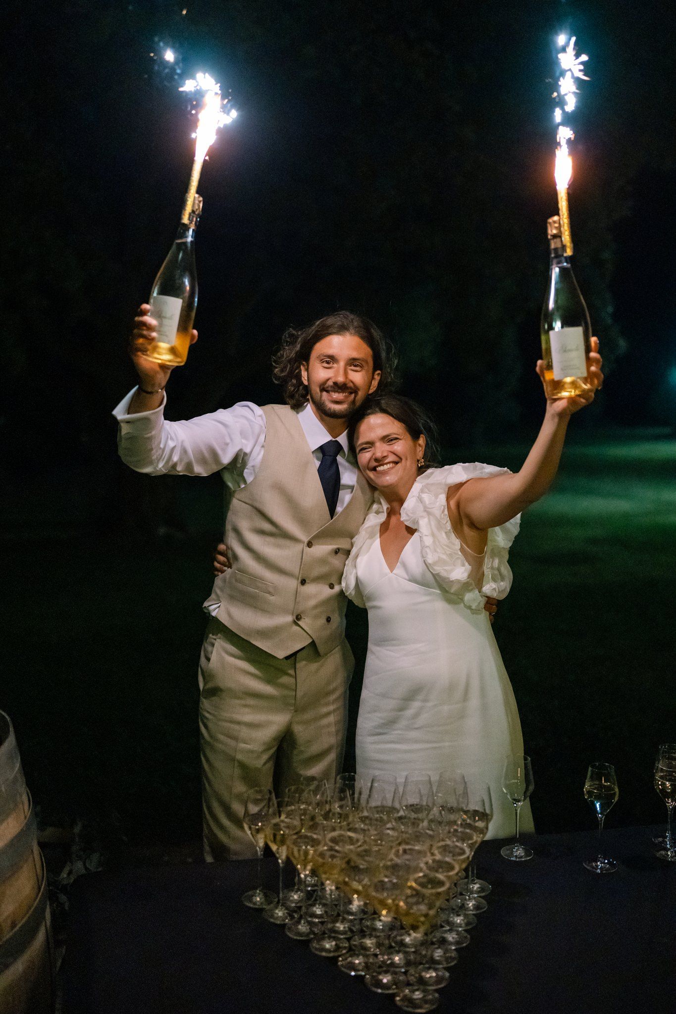 Couple celebrates with sparklers and champagne tower at outdoor reception.