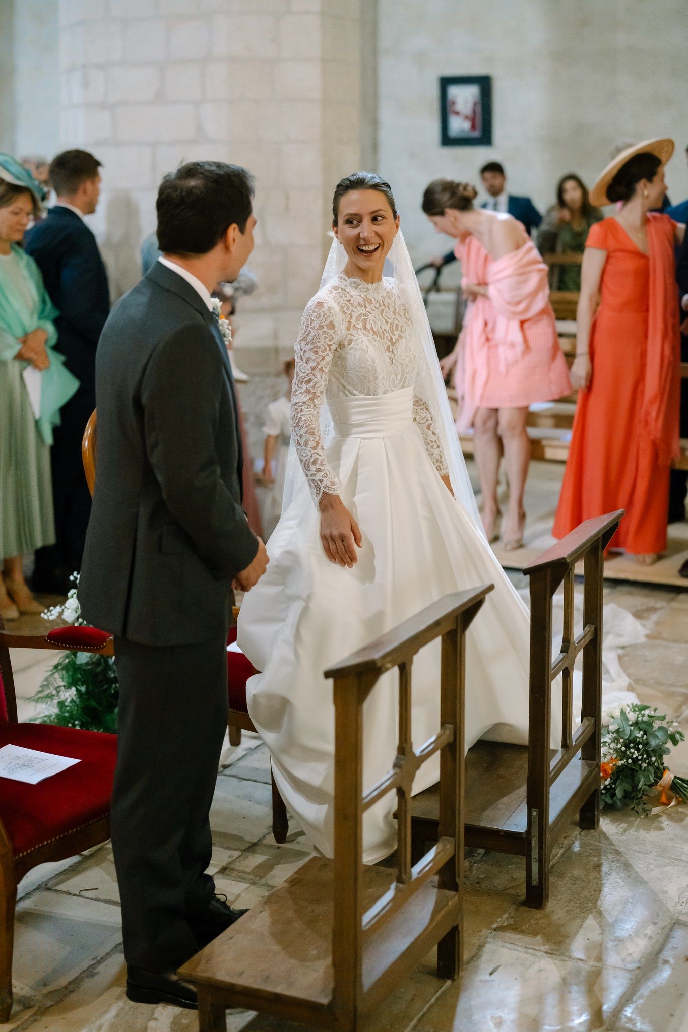 Bride in elegant lace wedding gown stands on church steps during ceremony.