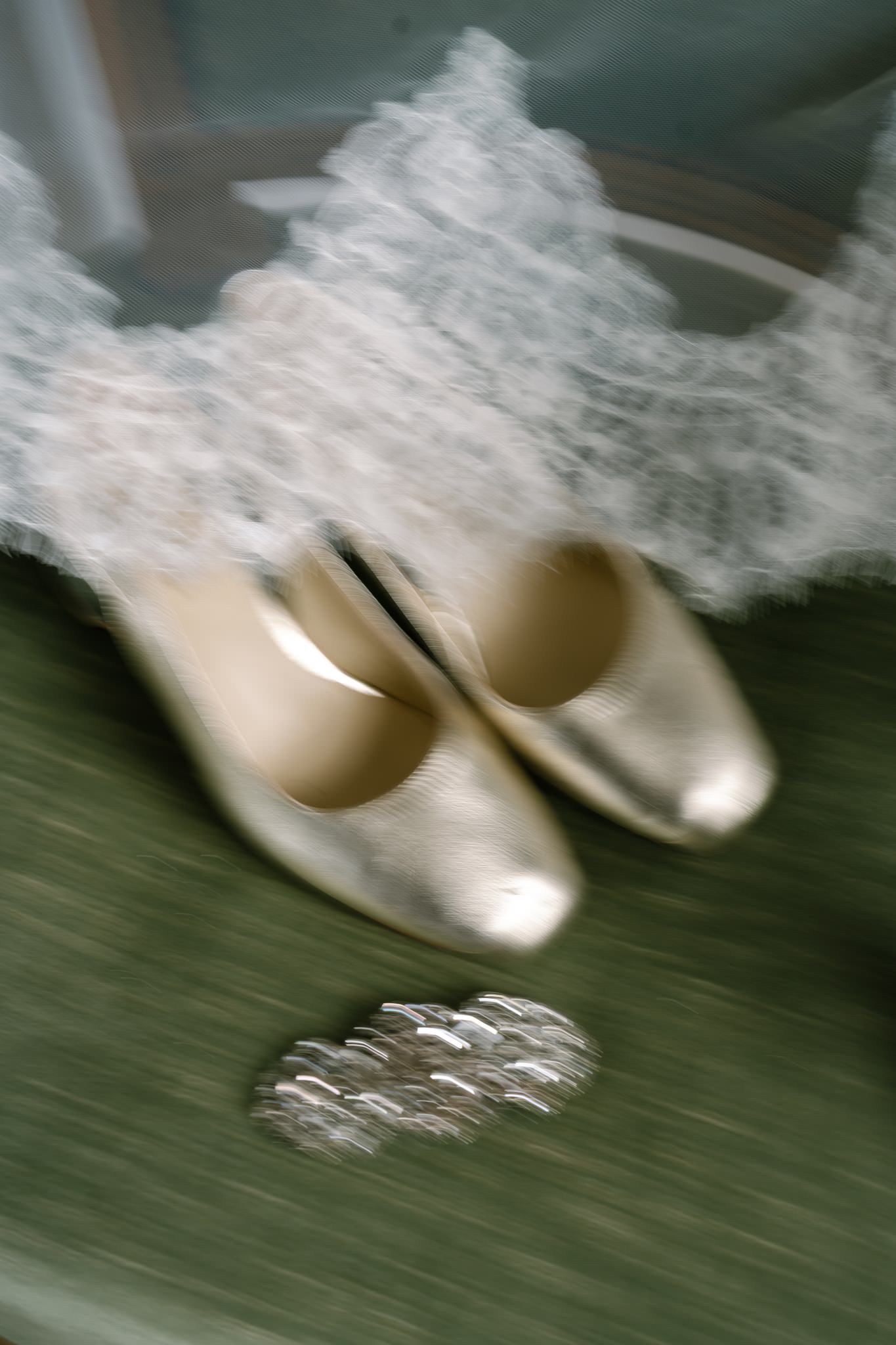 Motion-blurred image of white ballet or wedding shoes on a dark green surface.