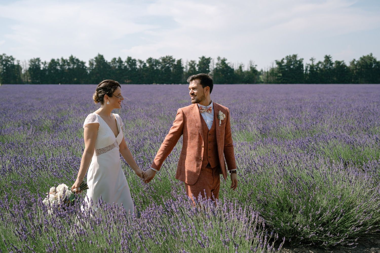 Couple walking through blooming purple lavender fields with mountains in the background.