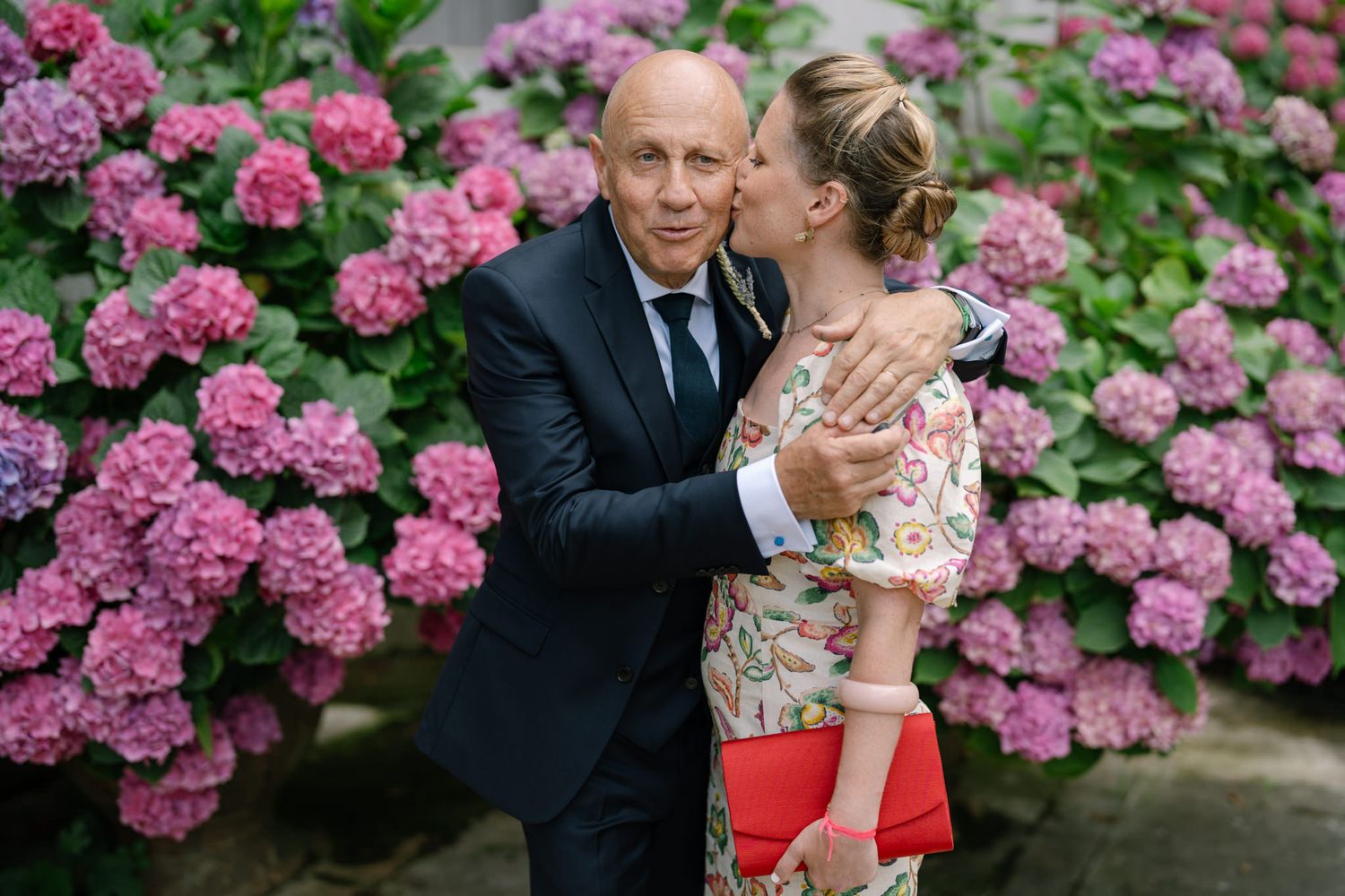 Couple embracing near vibrant pink hydrangea bushes in a garden setting.