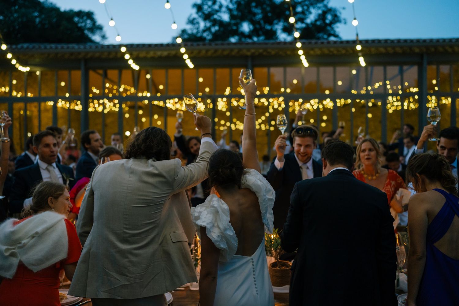 Guests celebrate under twinkling lights at an outdoor evening reception.