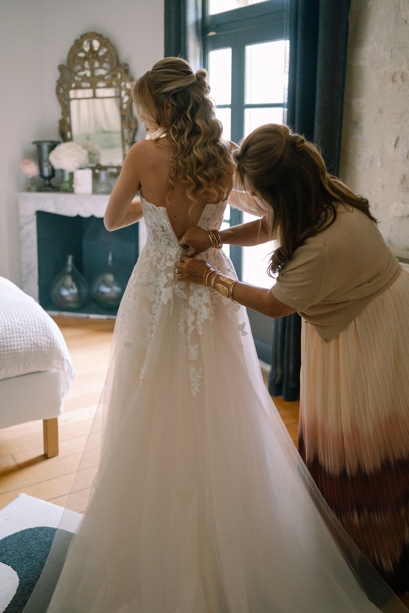 Wedding dress being adjusted in a sunlit room with vintage windows.